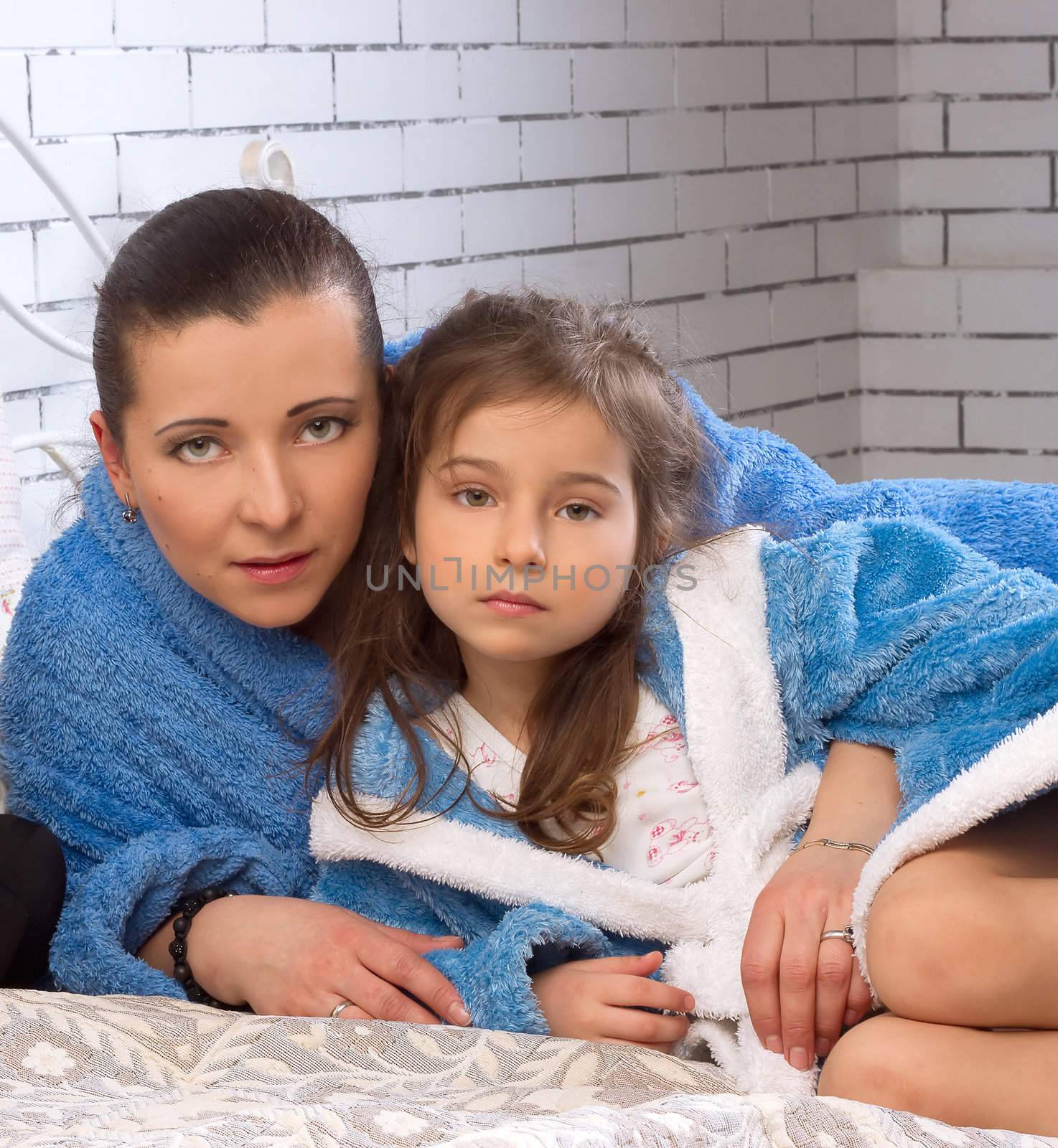 Mother and 5 year old daughter are in the same blue robes on the bed