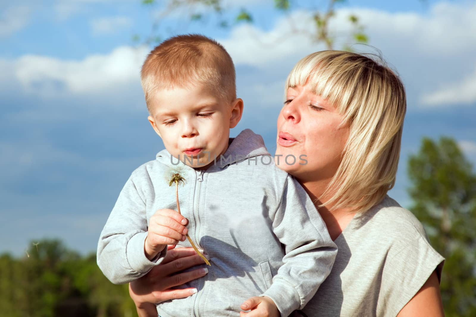 Kid and mother blowing dandelion. Spring time