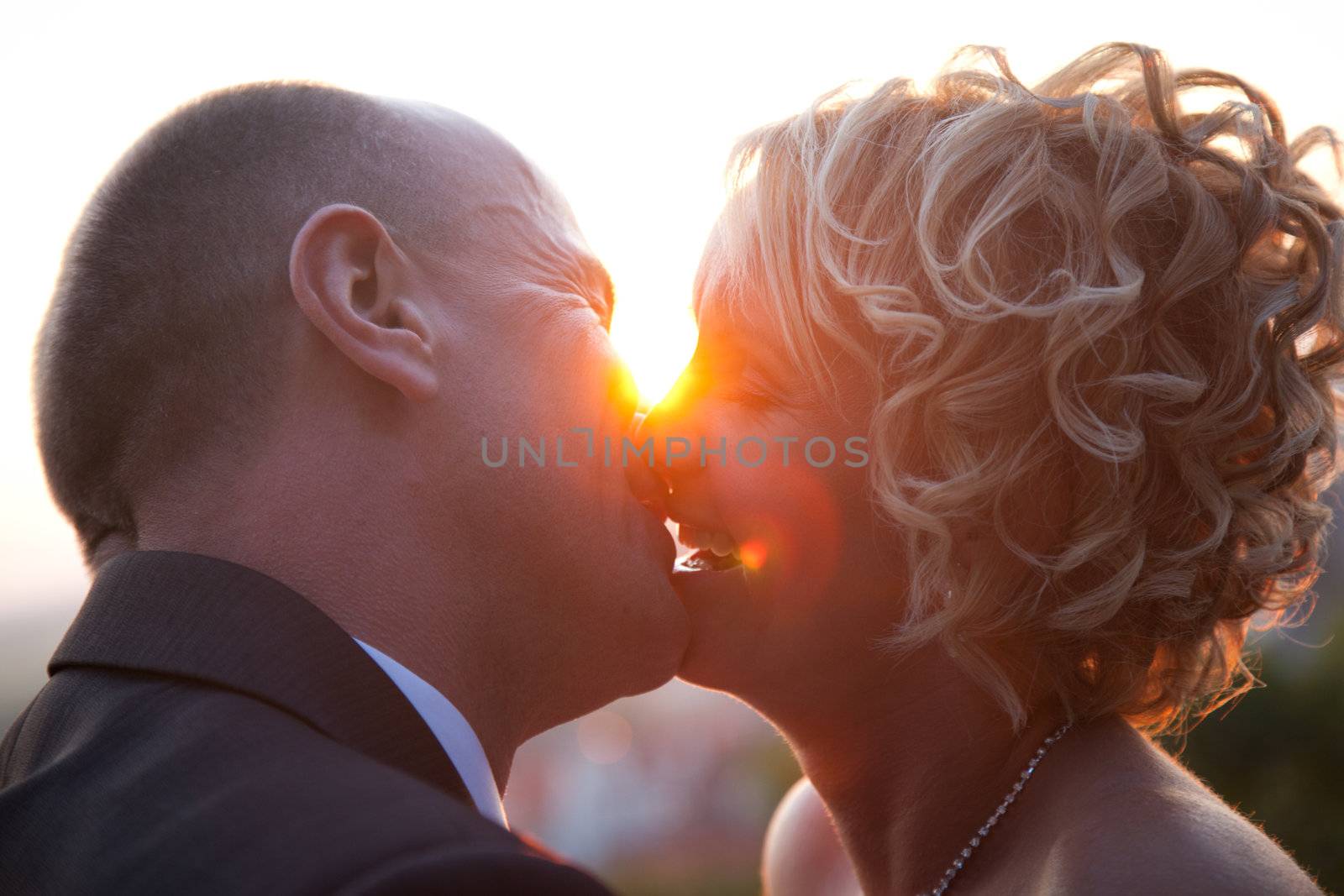 Happy bride and groom kissing outdoors at sunset