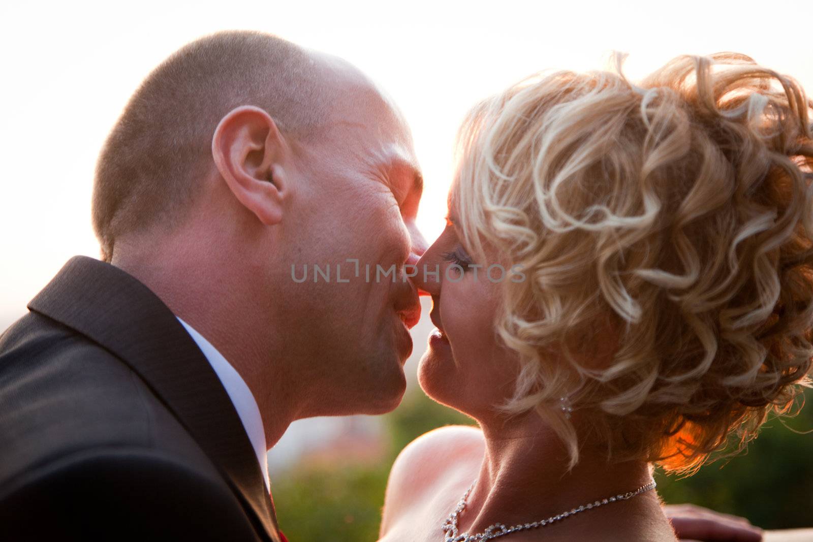 Happy bride and groom kissing outdoors at sunset