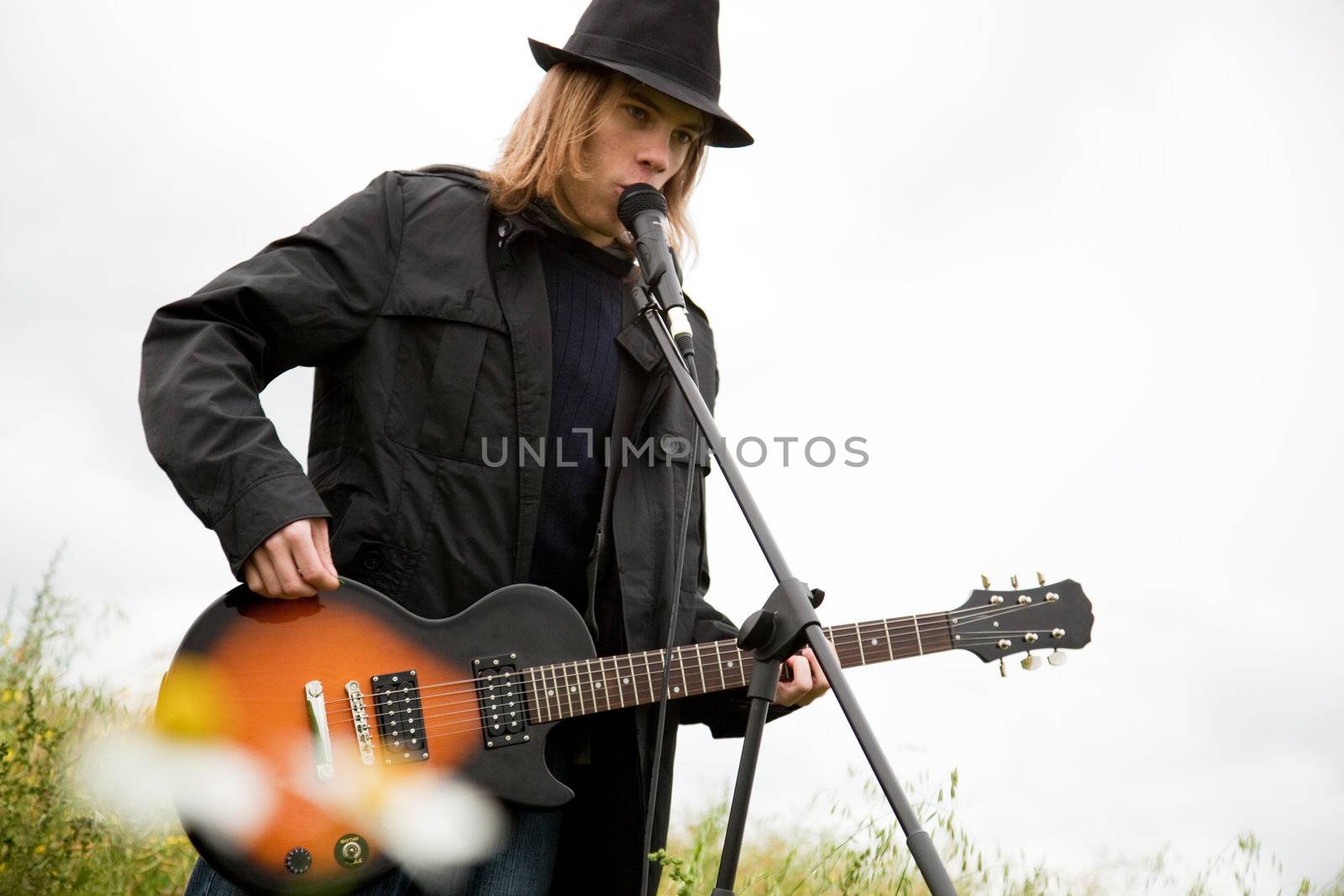 Man in hat playing guitar outdoors.