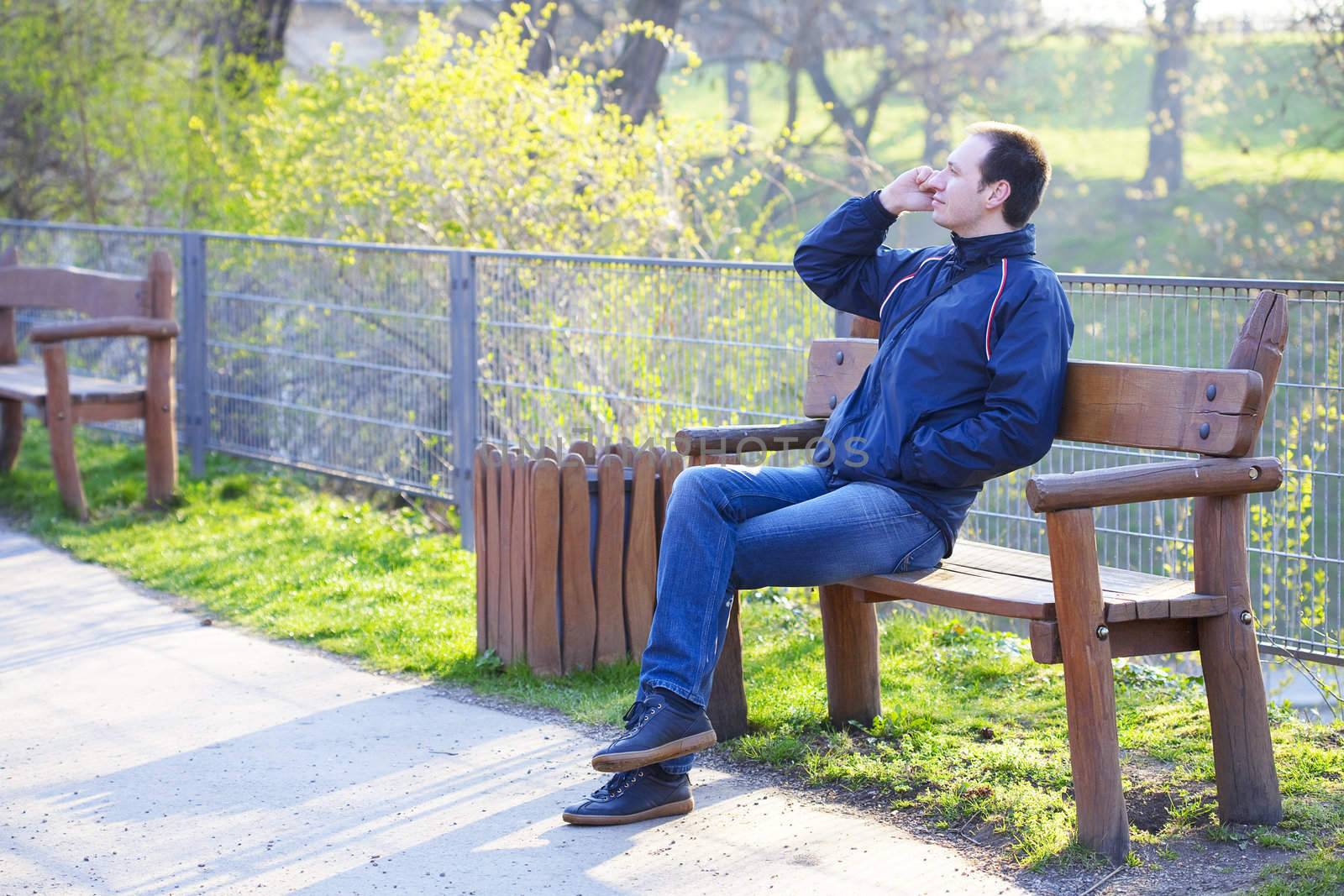 man sitting on a park bench talking on cell phone by jannyjus