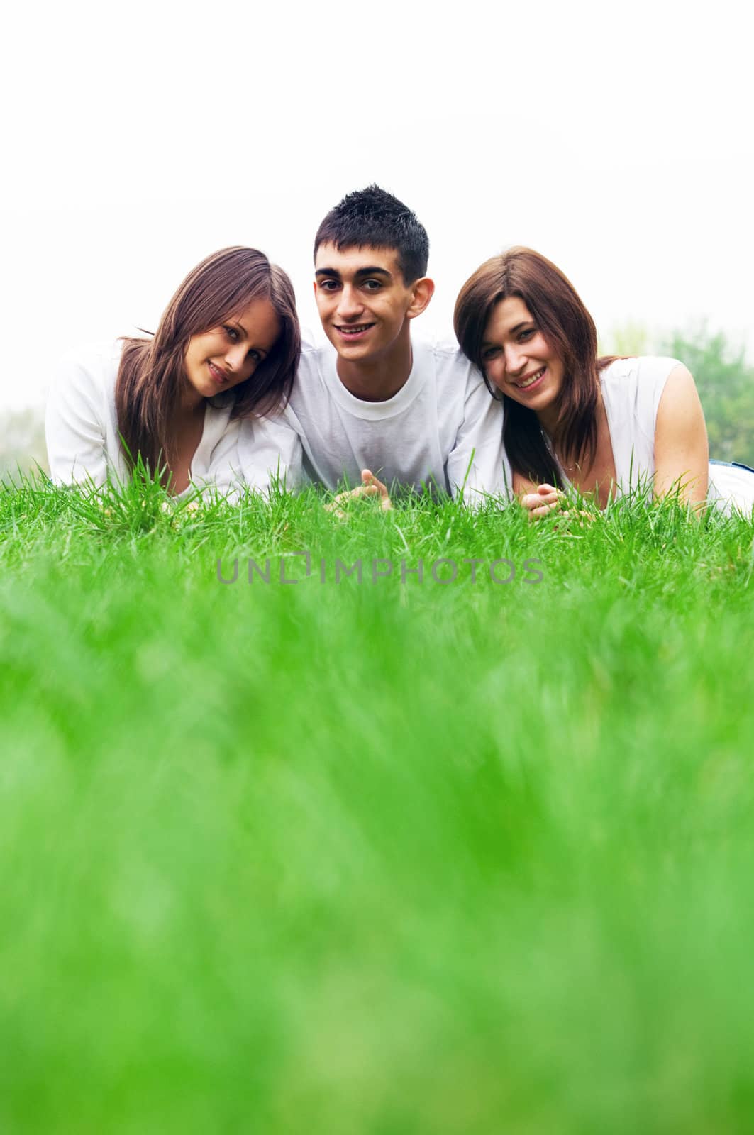 Three young happy friends lying together and smiling