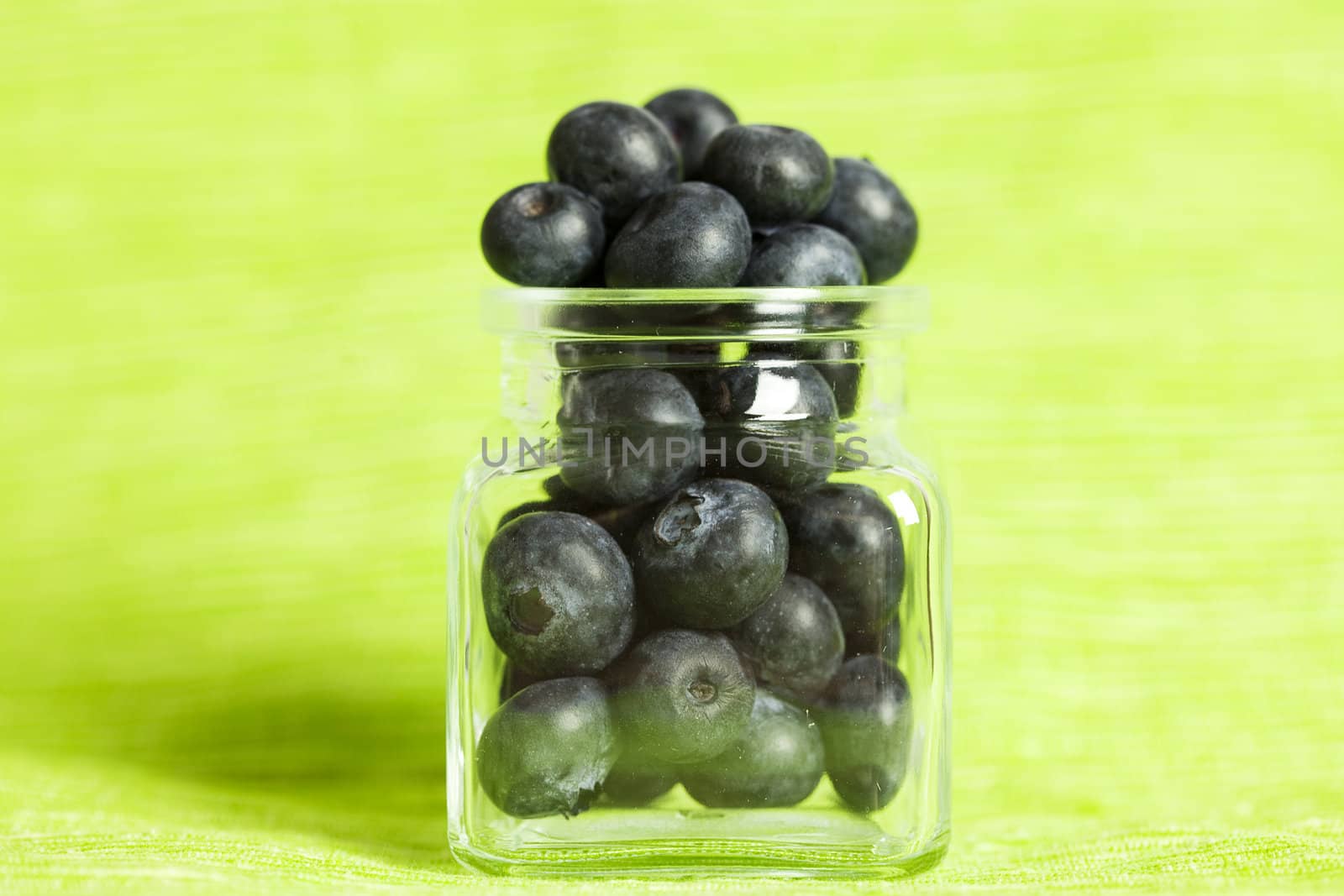 blueberries in a glass jar on a green background