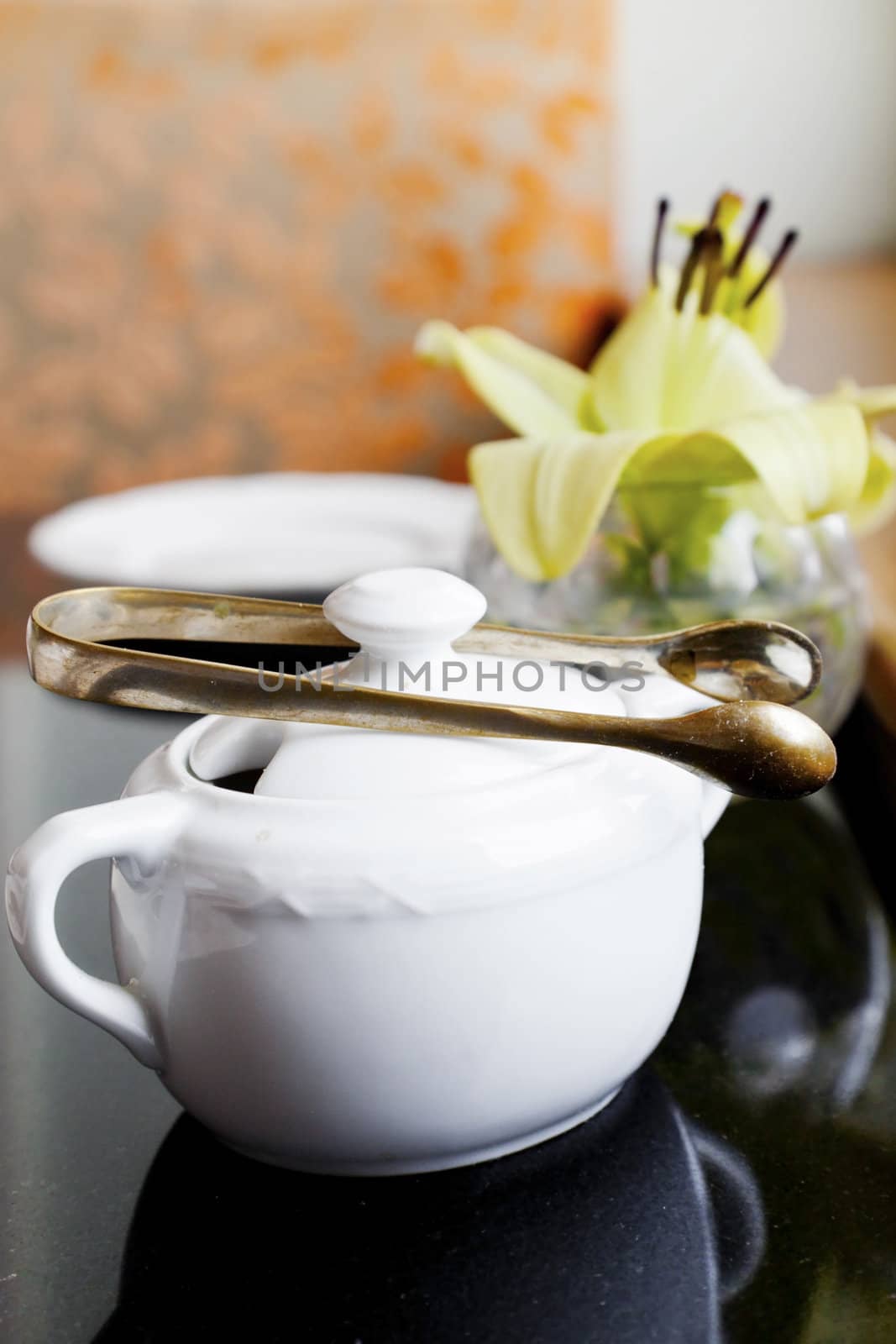 Vertical Interior corner detail of black top table with tea and coffee utensils of sugar bowls and bud vase with a lily by a window