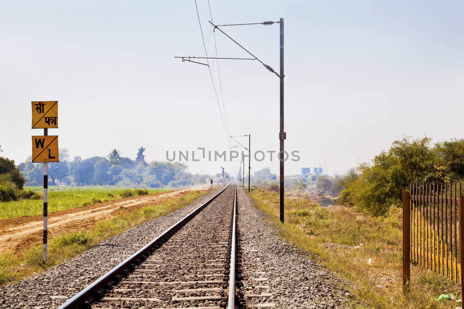 Horizontal landscape of railroad tracks in Indian cutting across the rural countryside along the outskirts of o Gujarat village towards the city of Surat. Typical scene with litter thrown around. Monotone