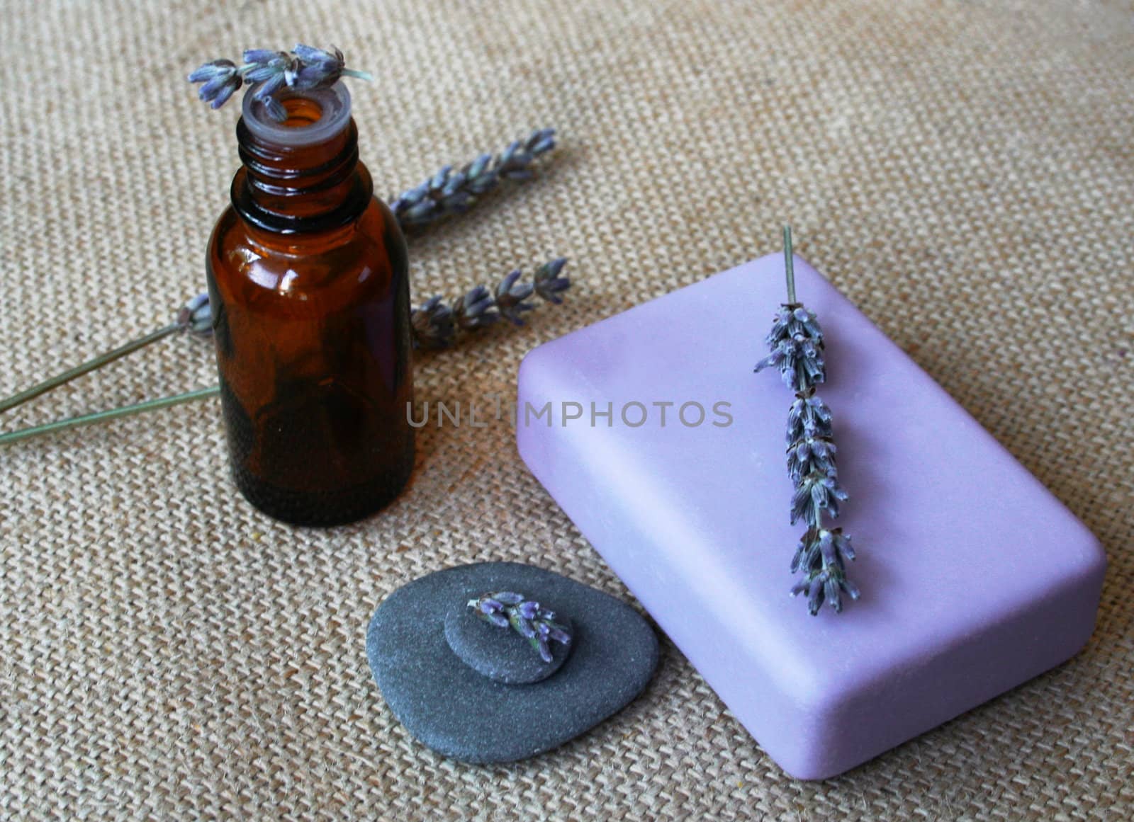 Lavender flowers, bottle of essential oil and soap on sackcloth background in a spa composition 