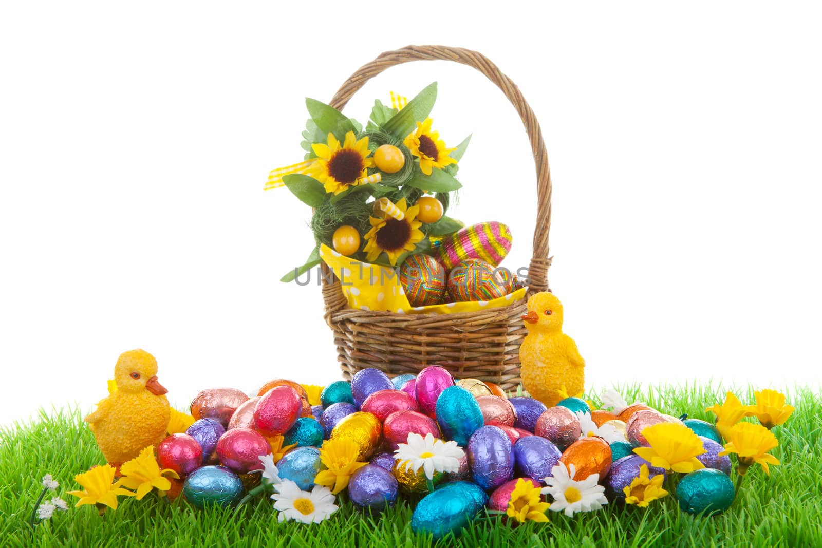 Colorful easter eggs, yellow chickens and basket on green grass with flowers