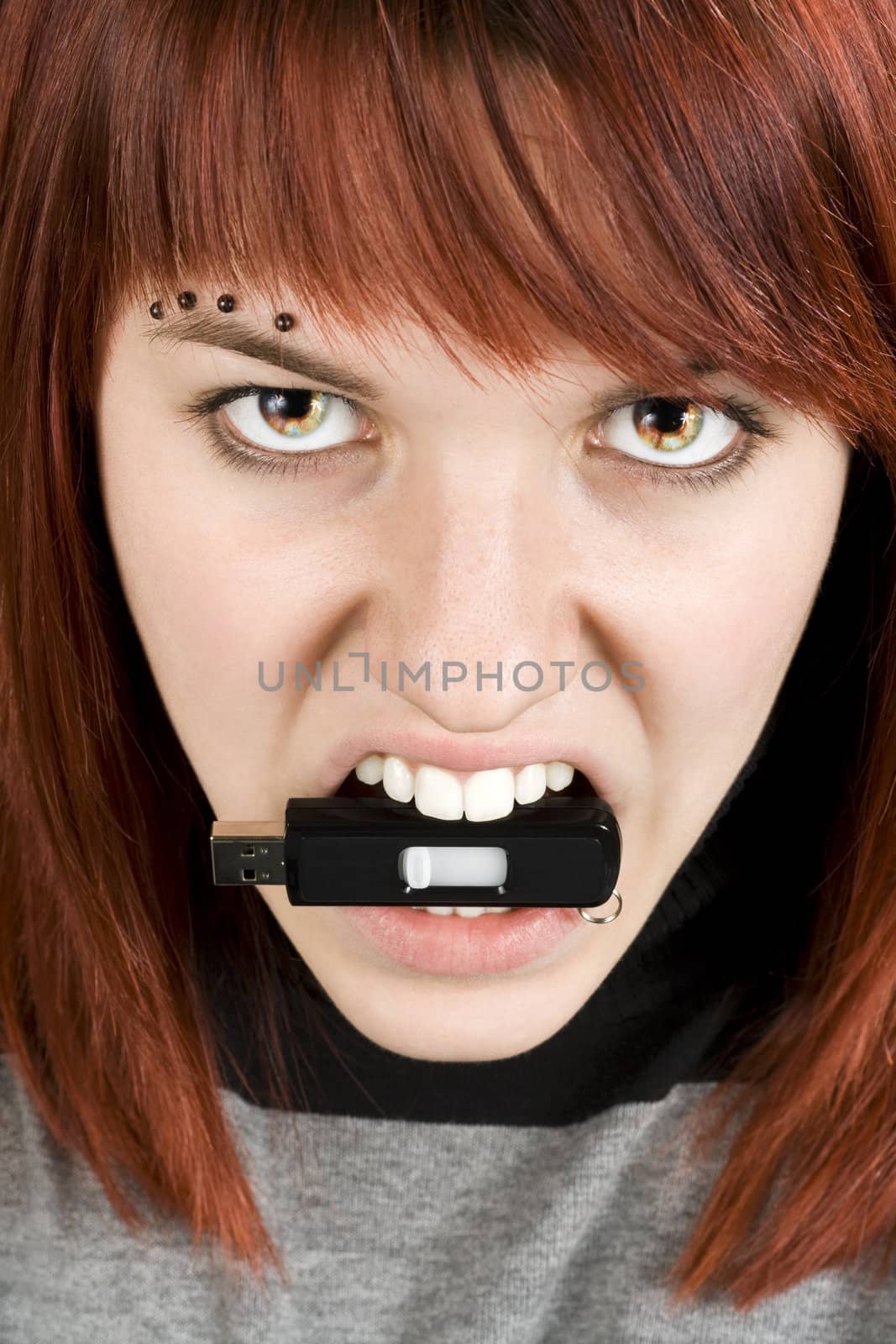 Beautiful redhead girl biting an usb memory stick with eyes on fire. Concept alluding to hate against computers or computer equipment.

Studio shot.