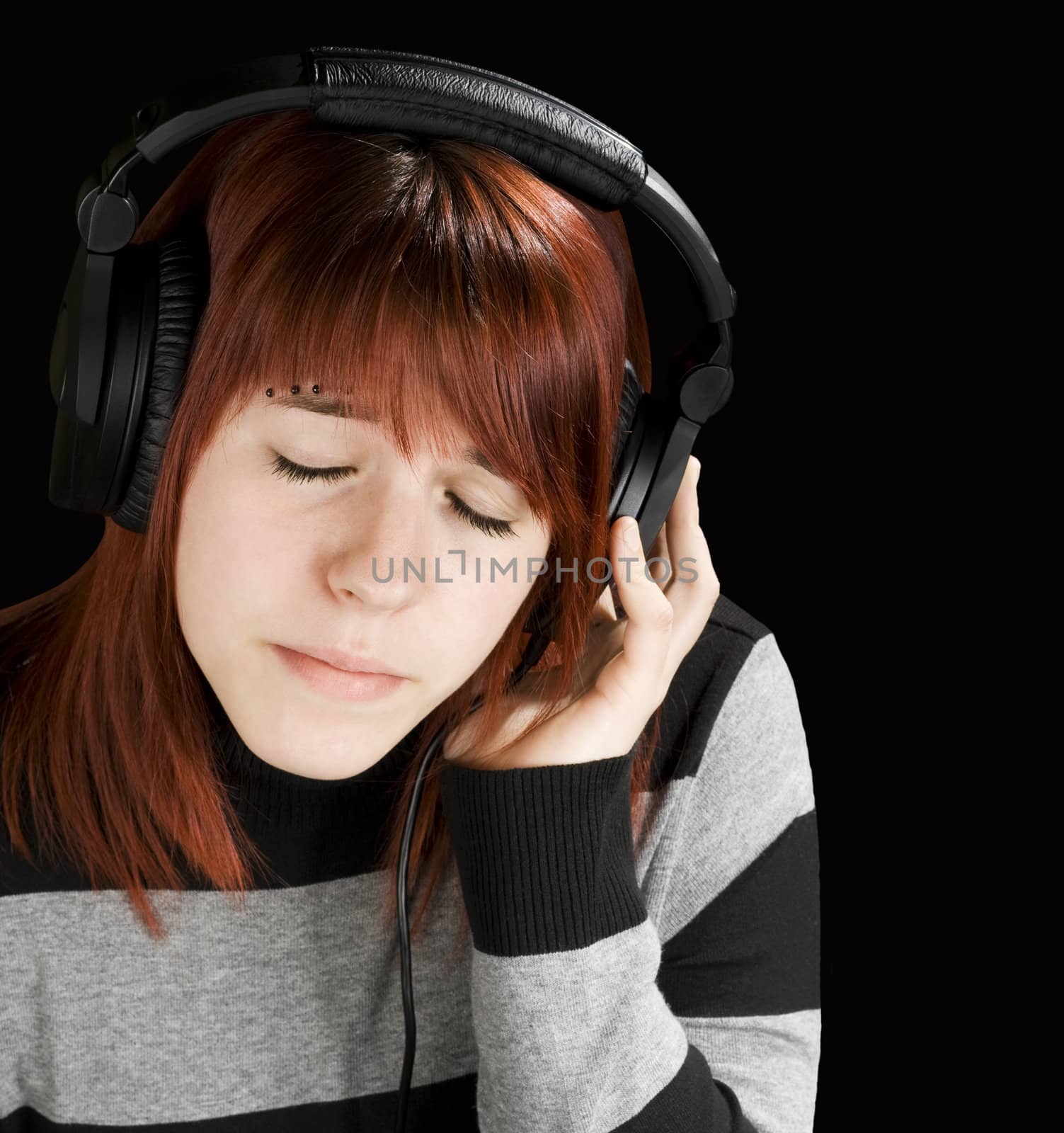 Beautiful redhead girl listening to music on headphones.

Studio shot.