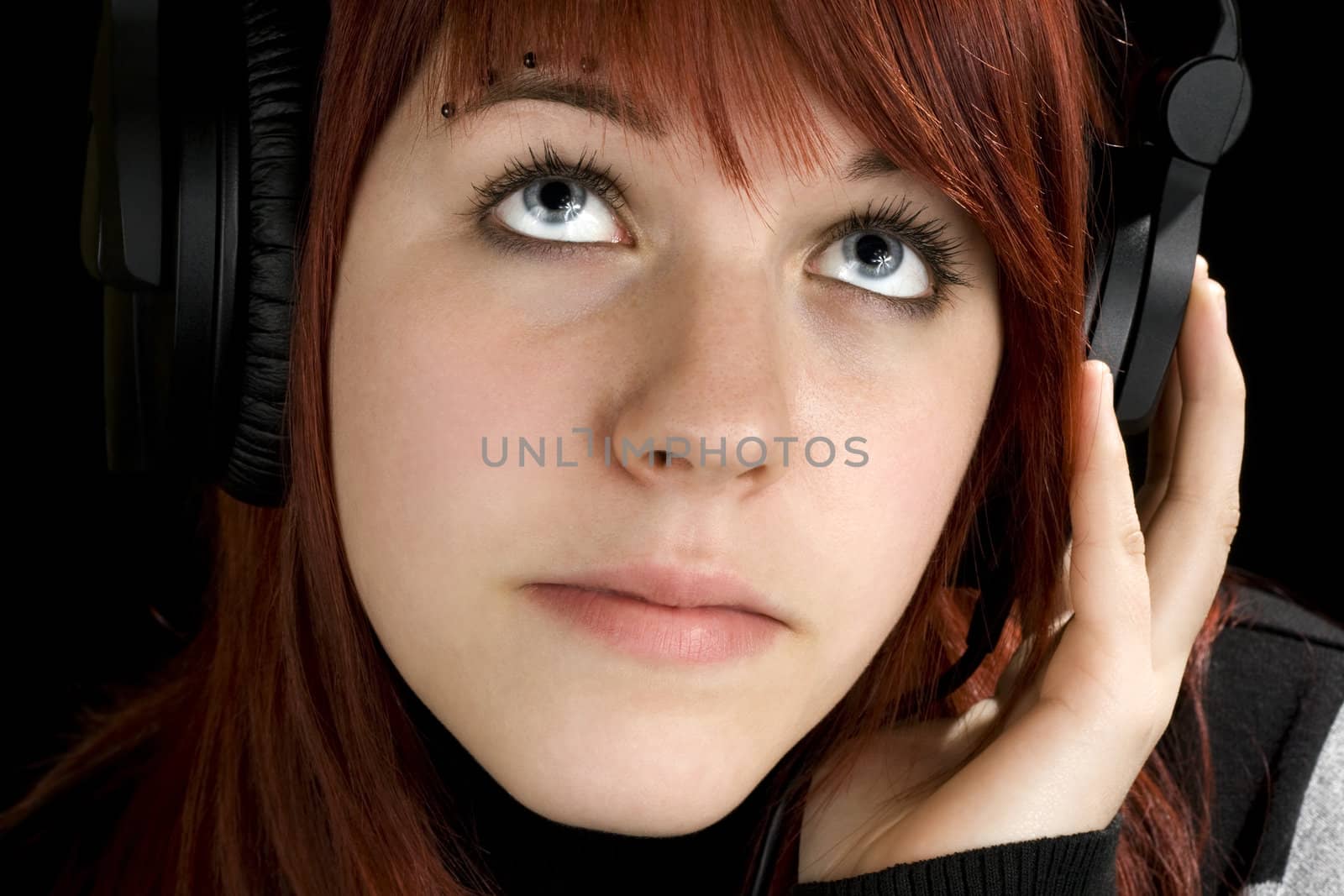 Pensive redhead girl listening to music and enjoying it (looking up, thinking).

Studio shot.