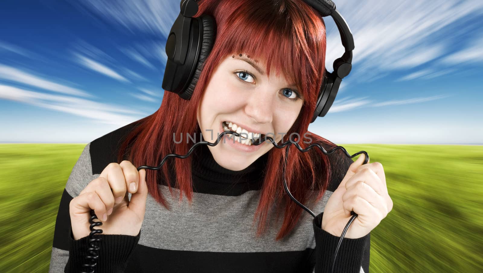 Cute girl with red hair biting the cord of her headphones while listening to music.

Studio shot.