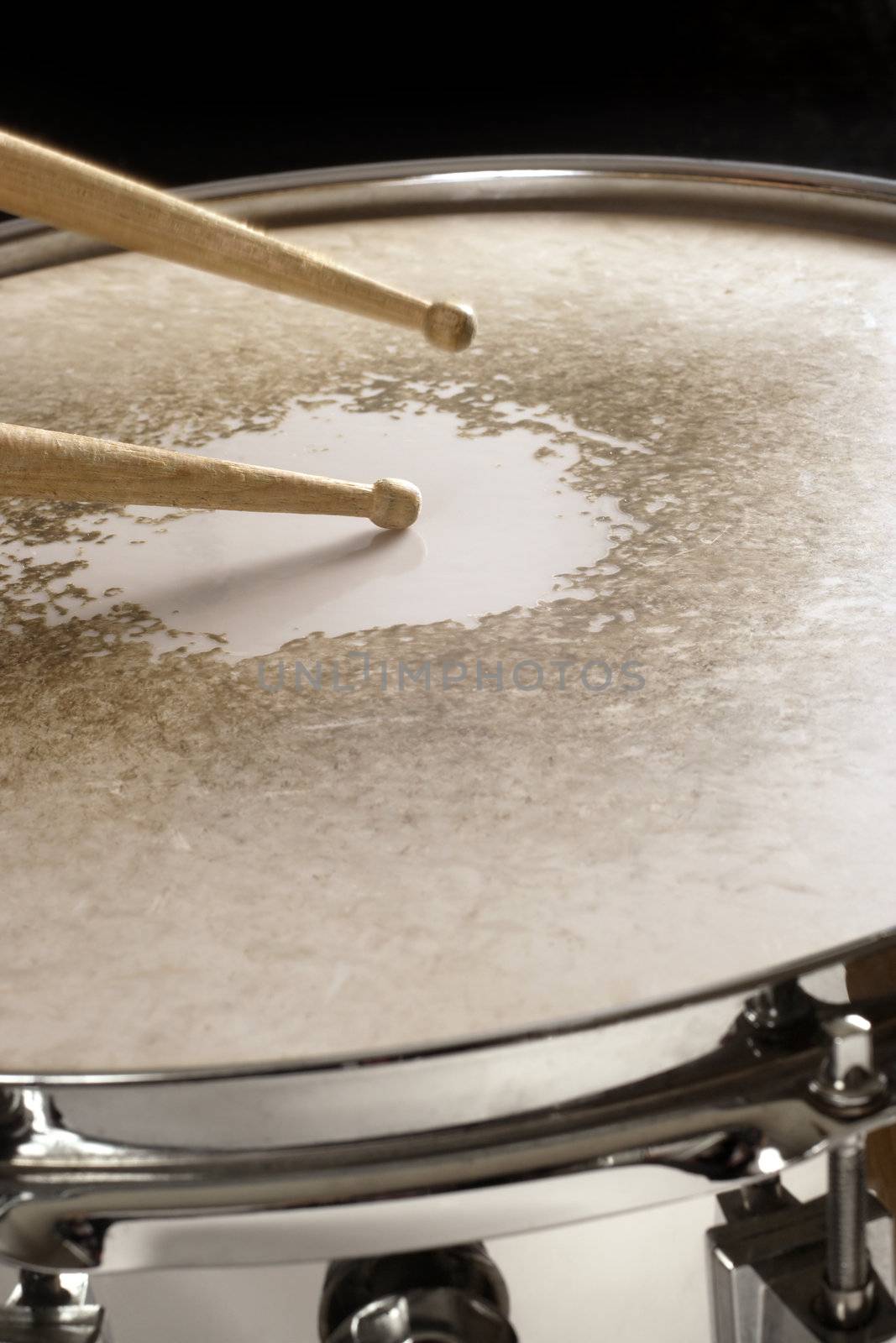 Drumsticks playing on a well-worn snare drum.