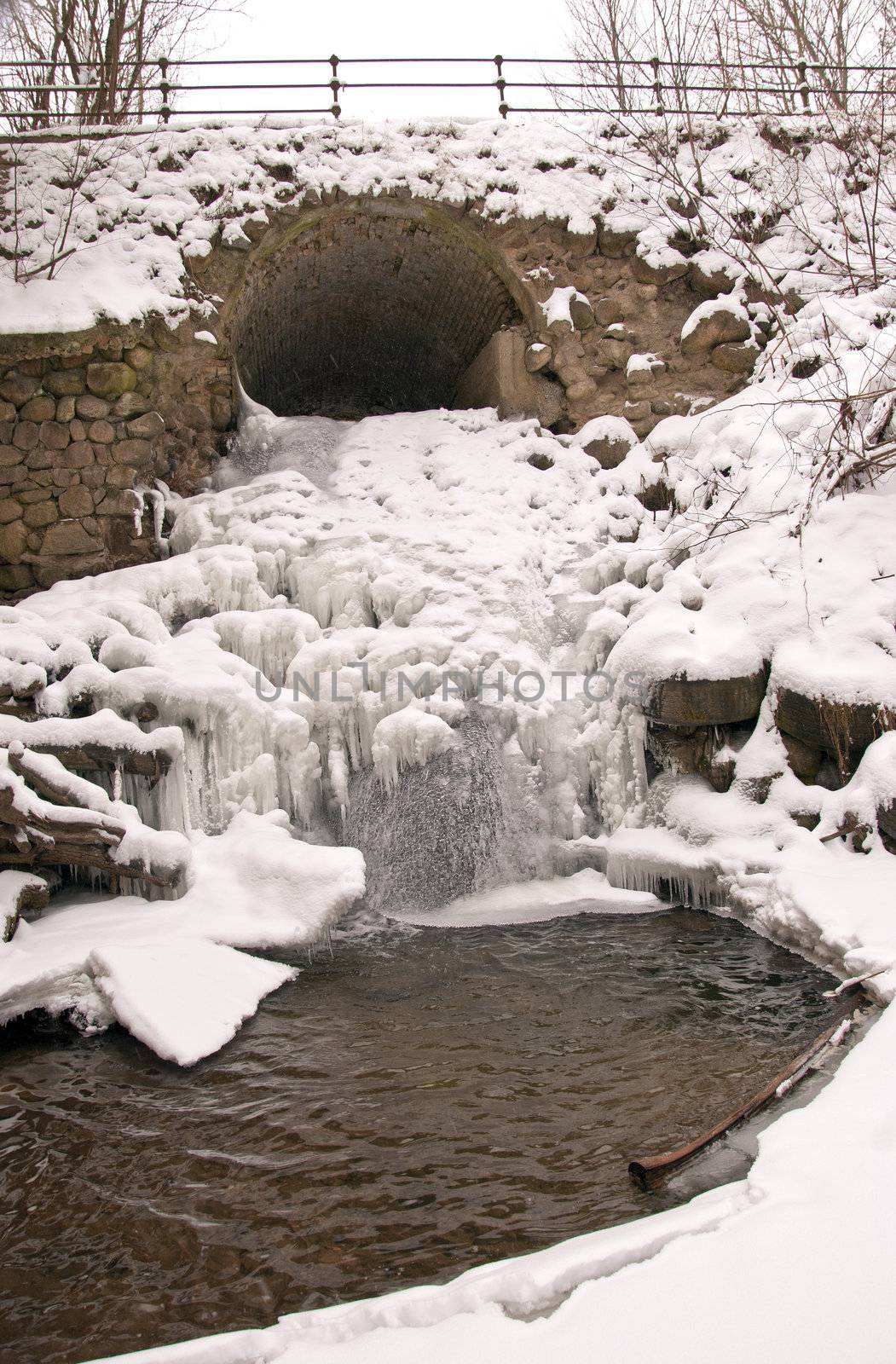 Stream water flow through arch waterfall ice icycles frozen in winter.