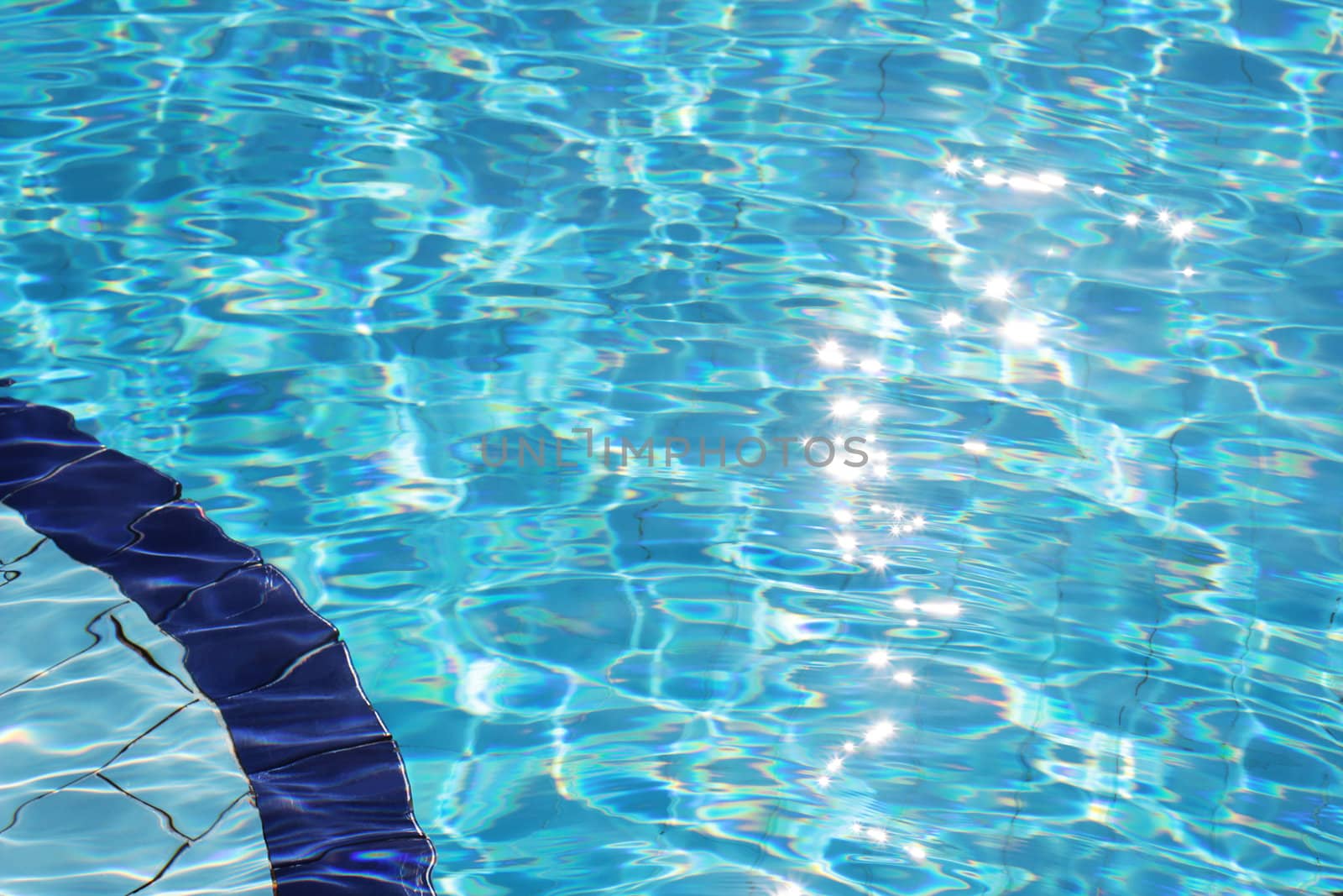 Clear blue water with sparkling sun reflections in an outdoor swimming pool.