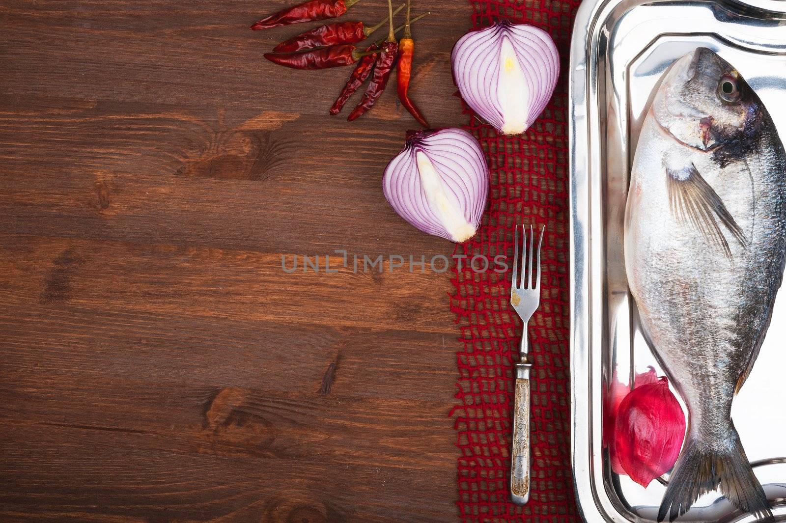 Dorado fish on a wooden surface with red onion and pepper