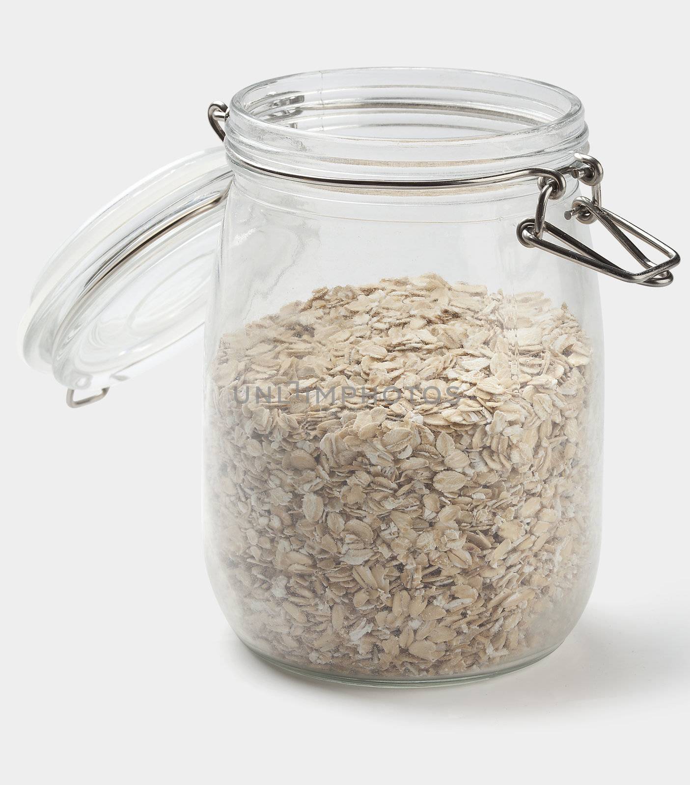 Oat flakes in the opened transparent jar on the white background