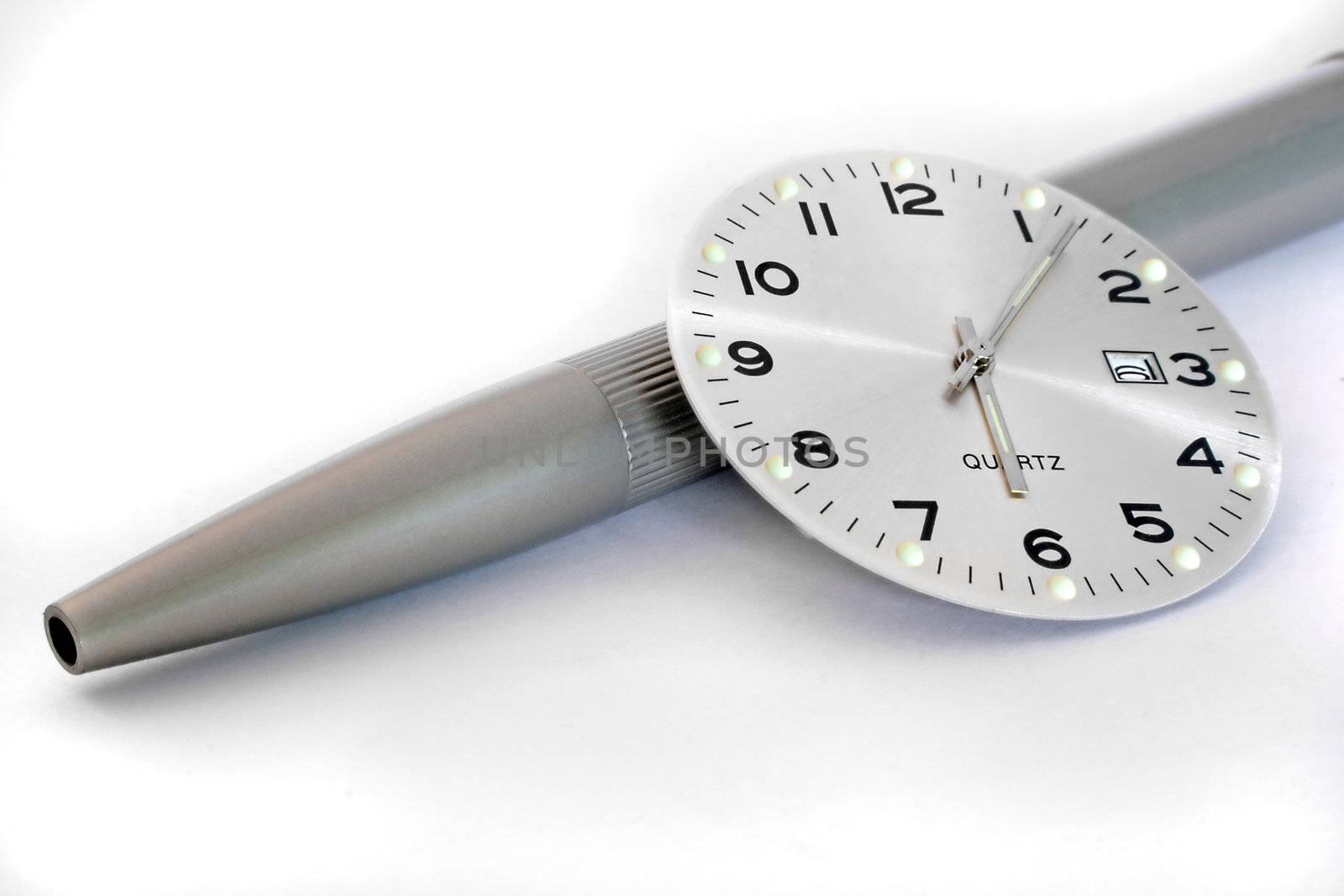 A close up of a clock face resting on an off-focus pen.