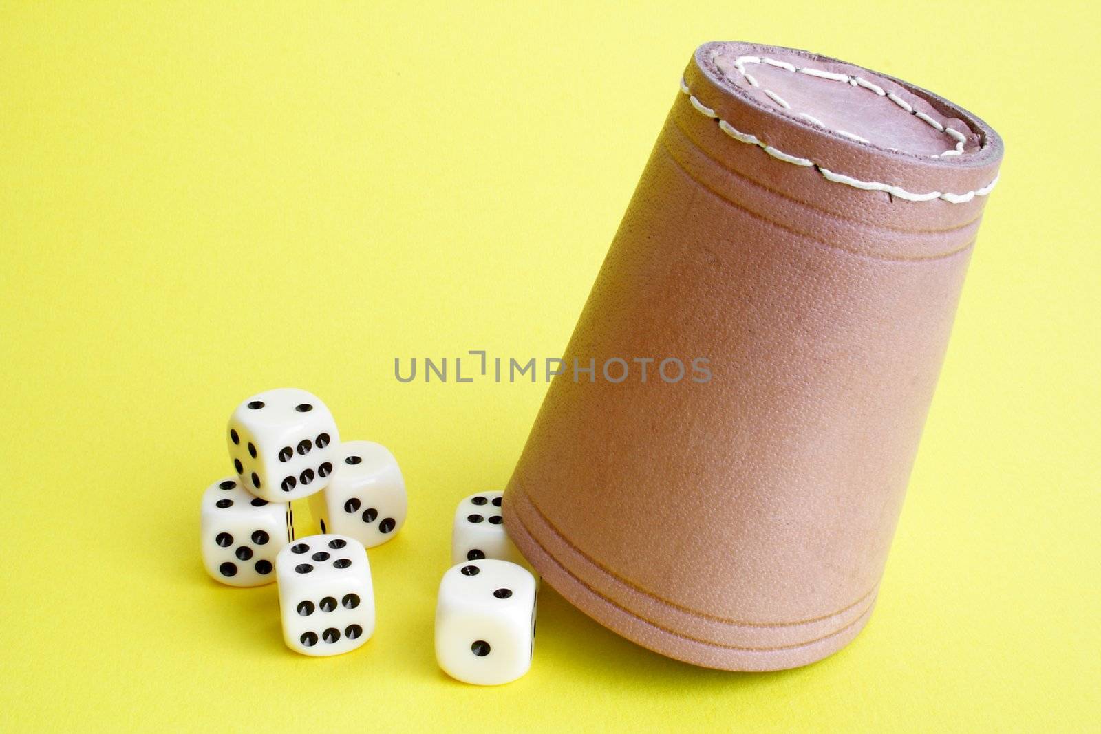 A dice shaker and several dices. All on a plain yellow background.