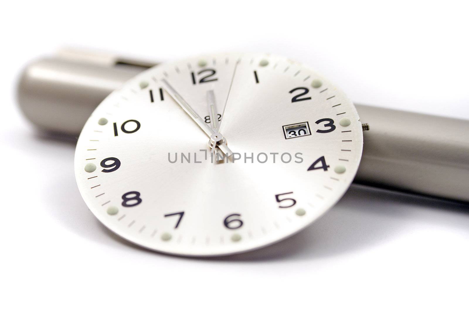 A close up of a clock face resting on an off-focus pen.