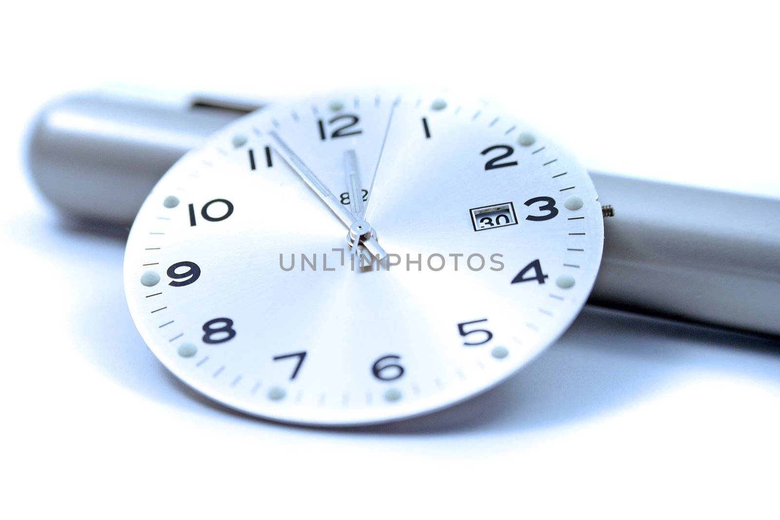 A close up of a clock face resting on an off-focus pen.