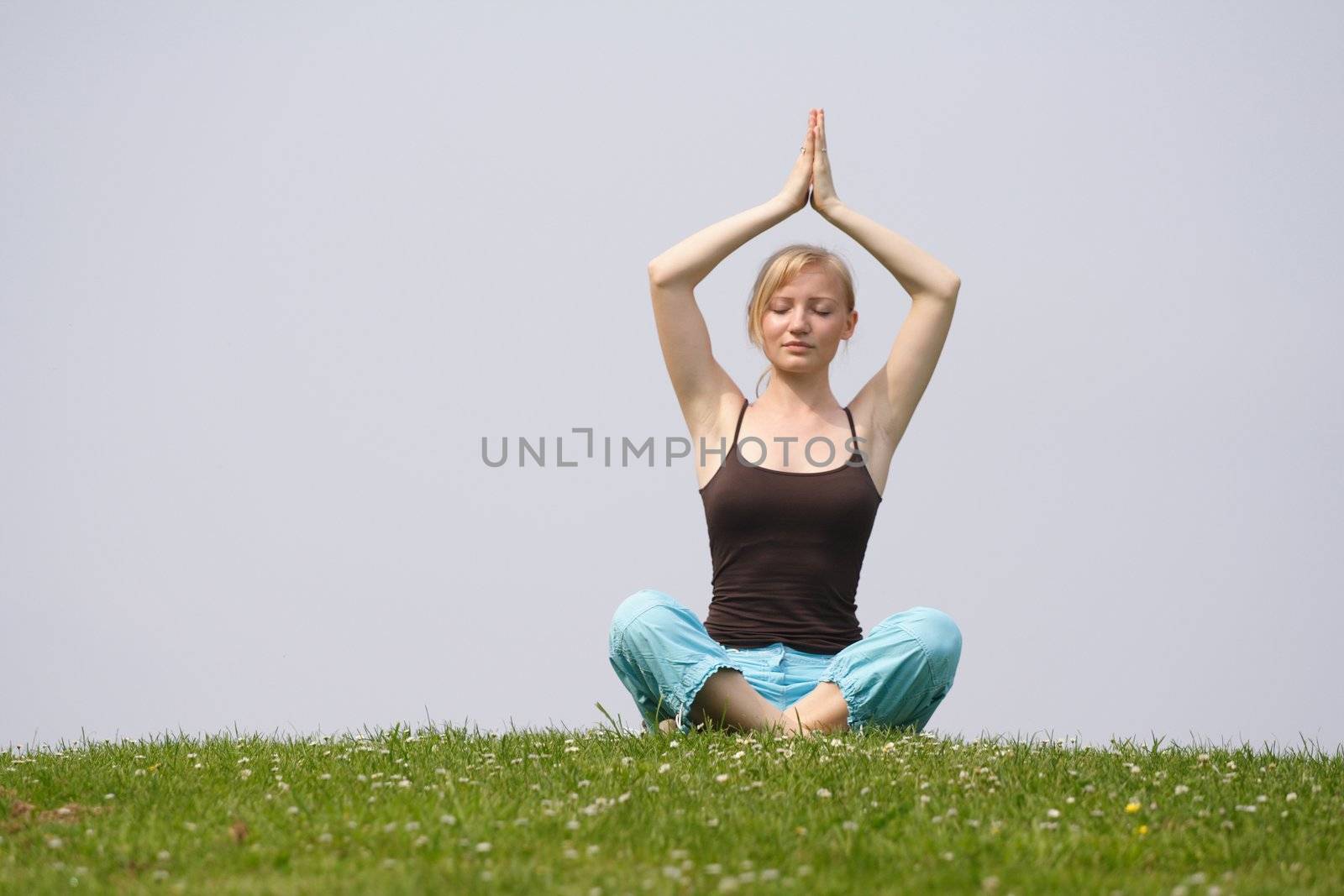 A young handsome woman doing yoga on a meadow.