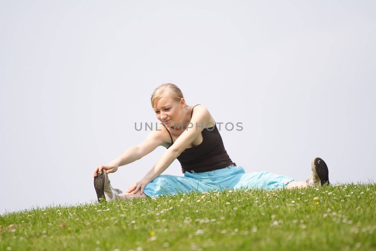 A young handsome woman doing gymnastics on a meadow.