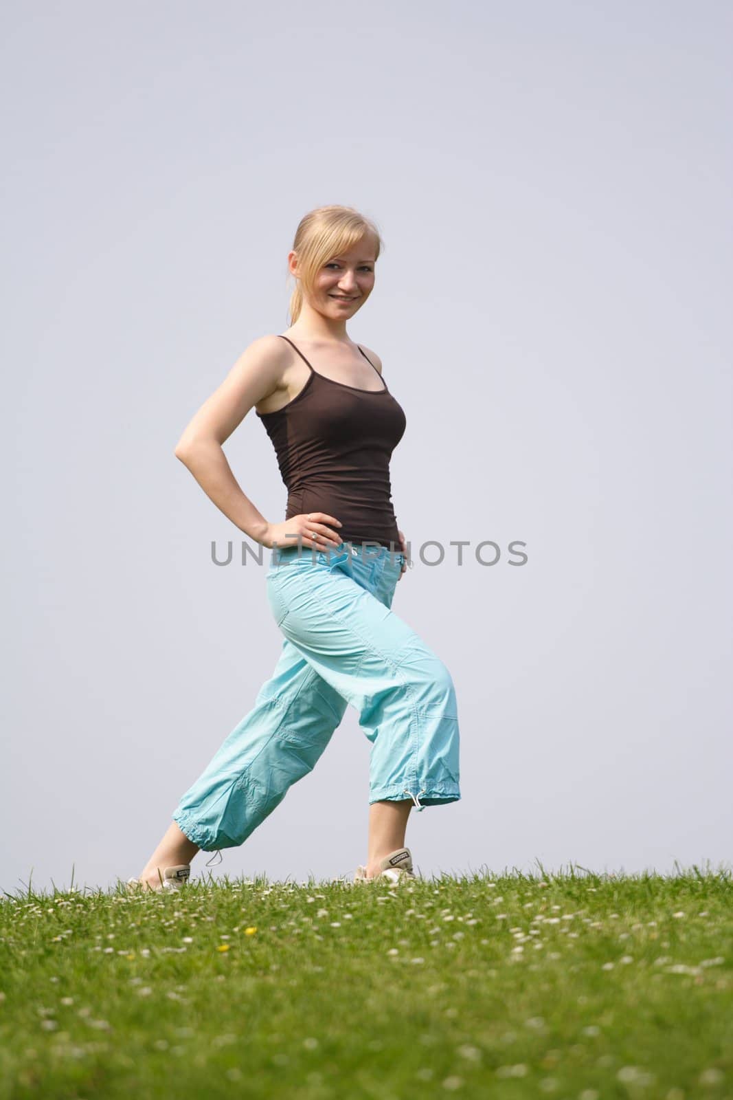 A young handsome woman doing gymnastics on a meadow.