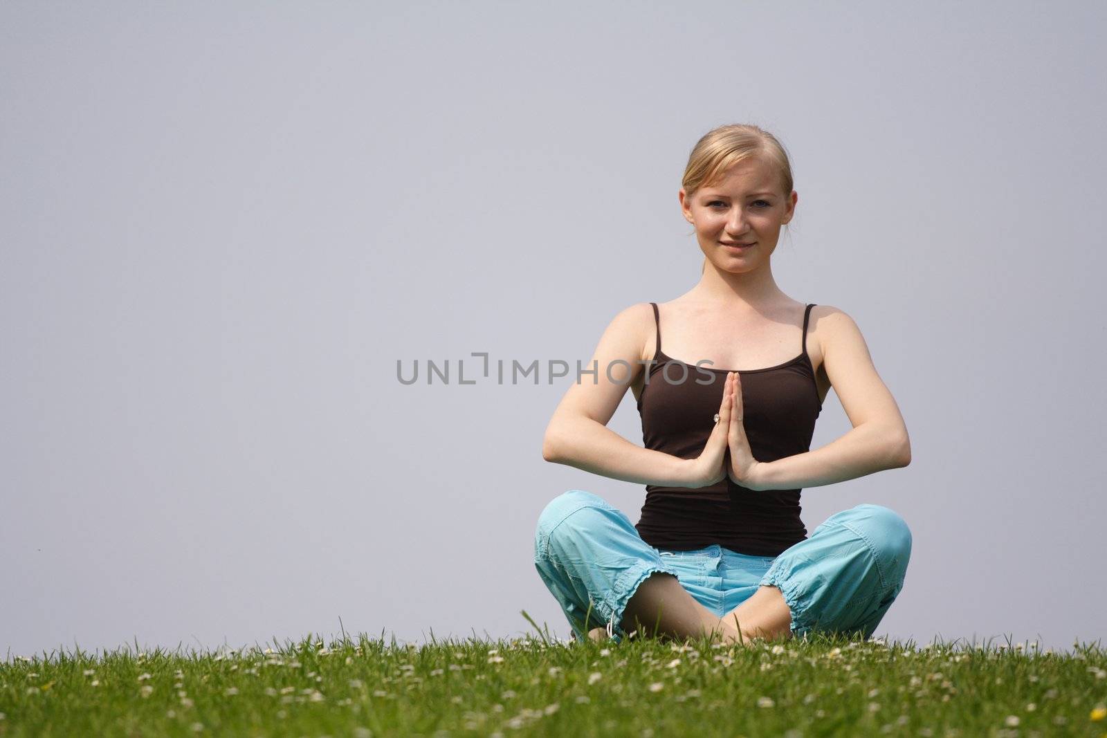A handsome young woman doing yoga on a green meadow.