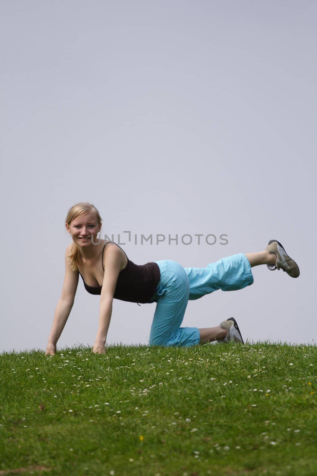 A young handsome woman doing gymnastics on a meadow.