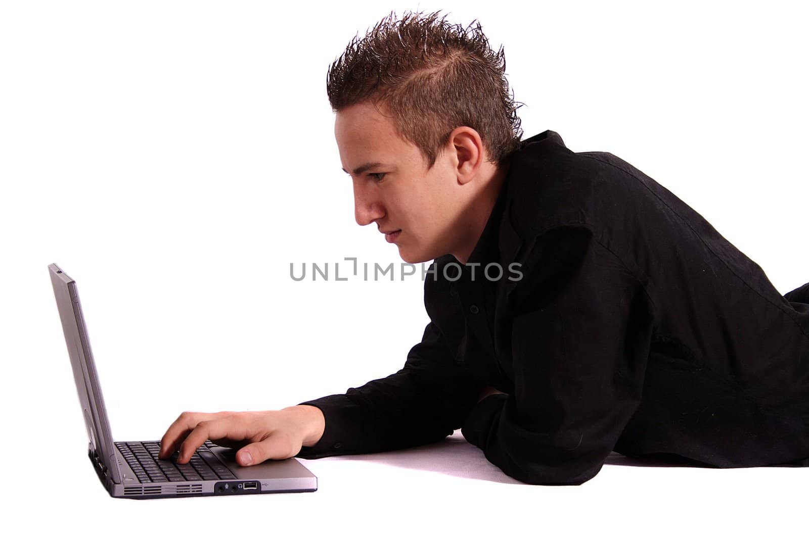 A young handsome man lying on the floor and surfing the internet with his notebook computer. All isolated on white background.