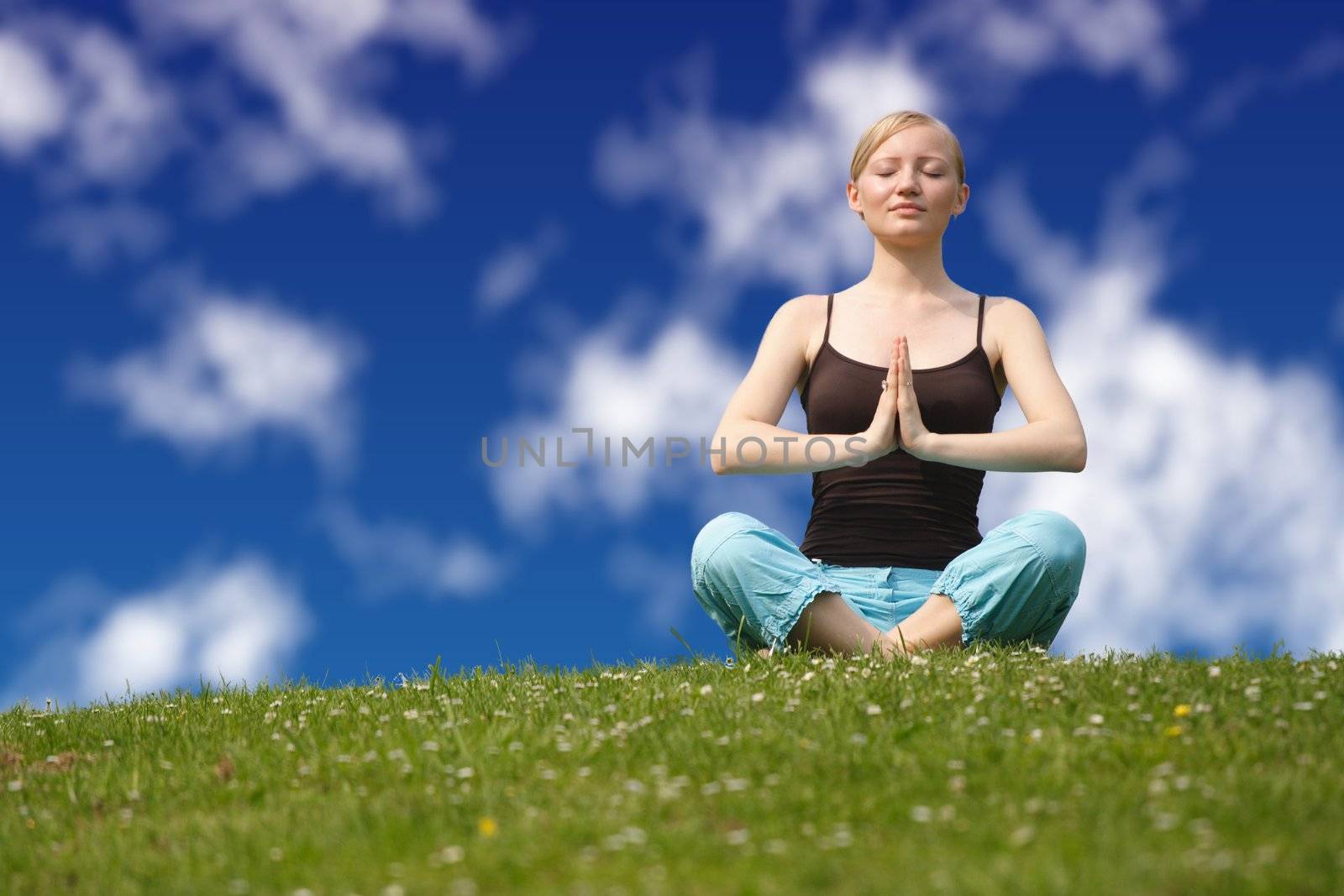 A young handsome woman doing gymnastics on a meadow infront of a bright blue sky.