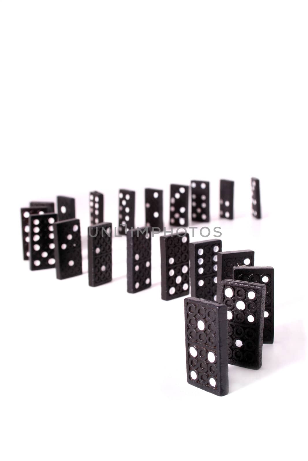Several dominoes standing one after another in front o a white background.