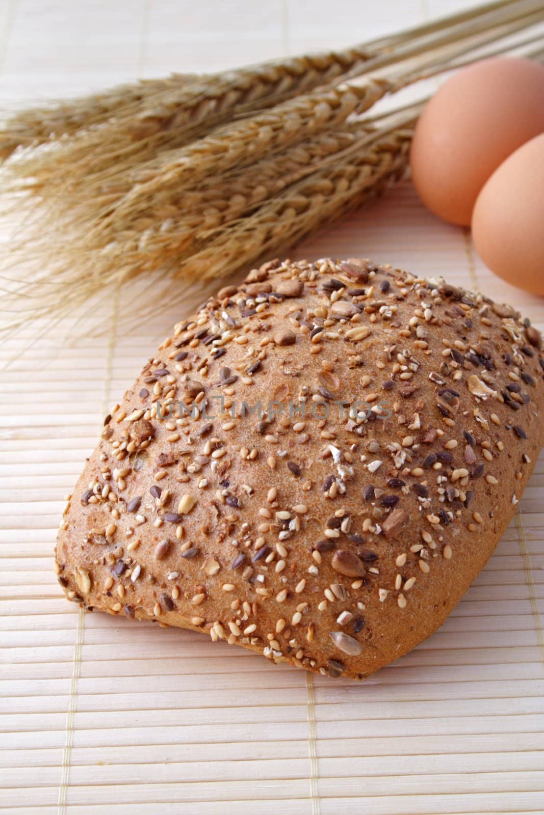 A whole-grain roll lying next to some eggs and grain.