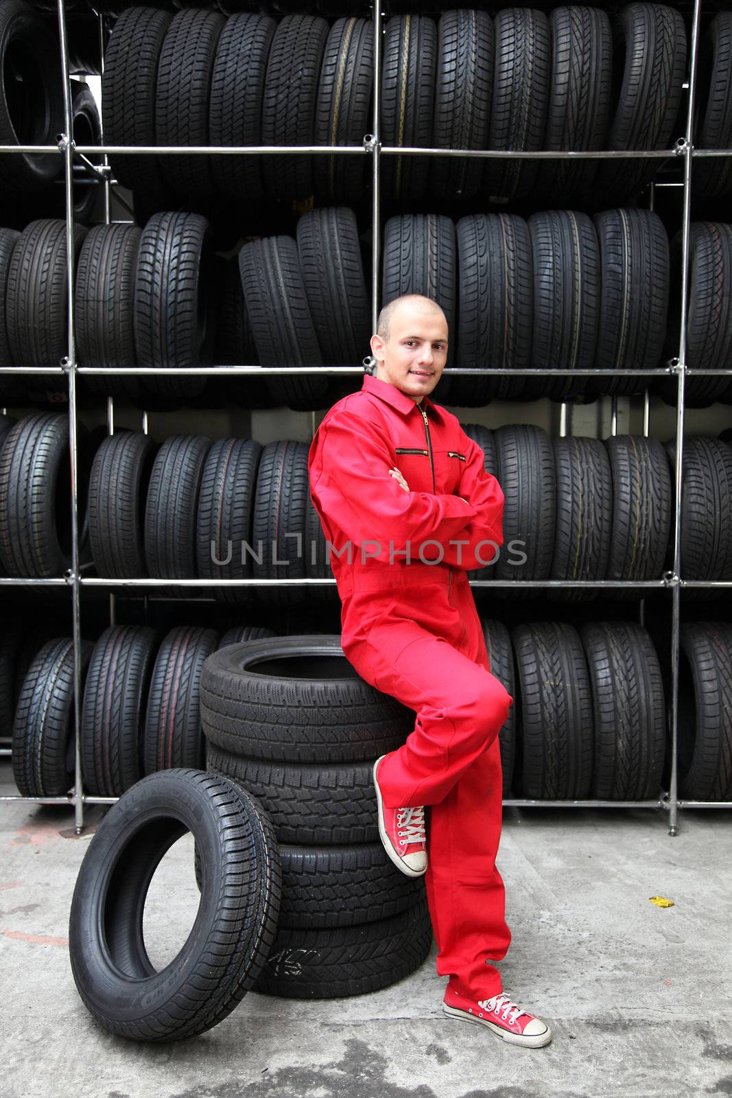 An optimistic mechanist standing next to pile of tires.