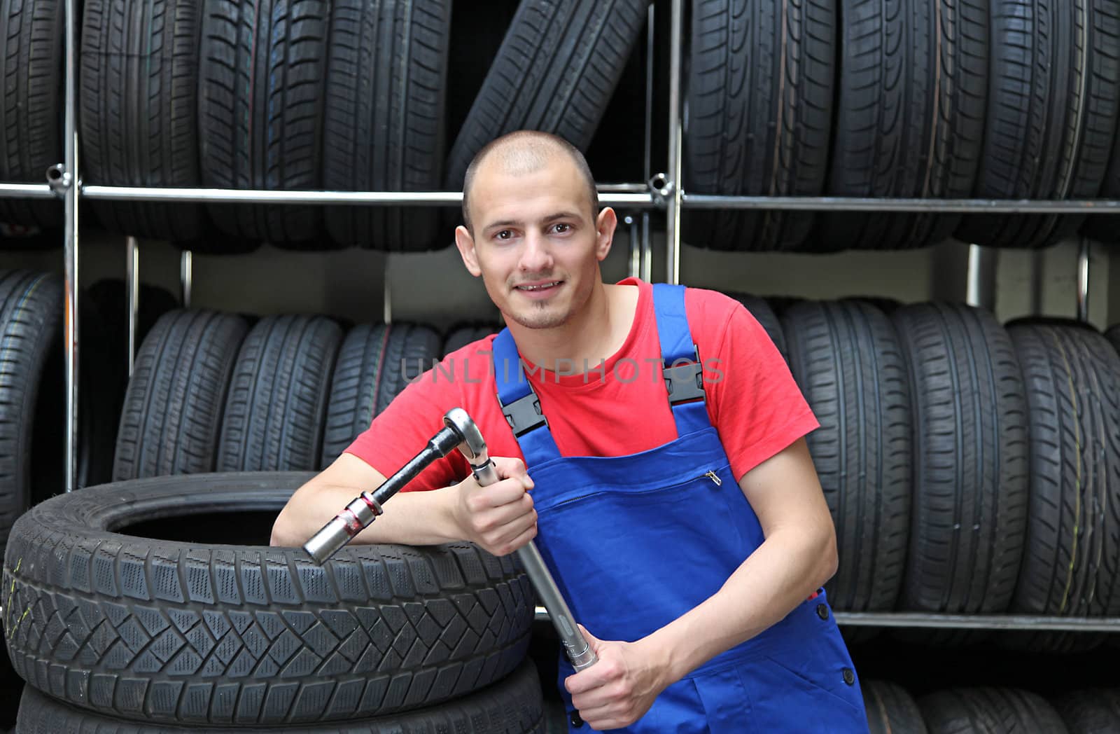 An optimistic mechanic standing in front of a rack full of tires.