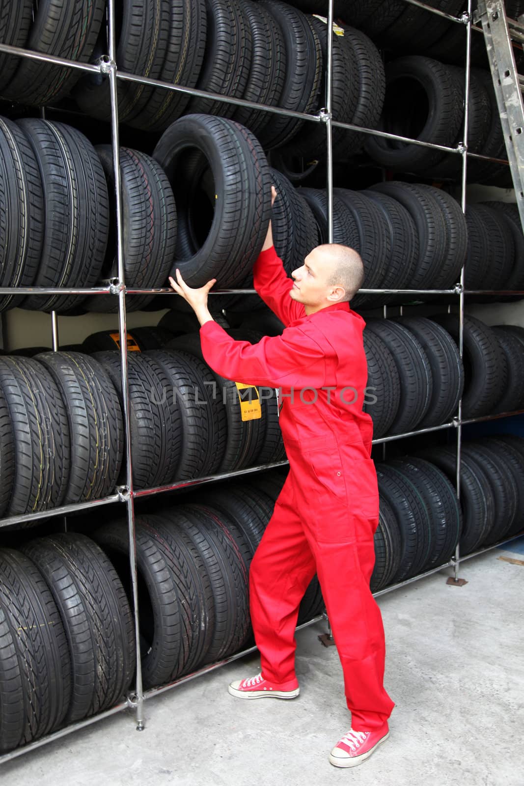 A working mechanic in a garage standing next to a rack full of tires.