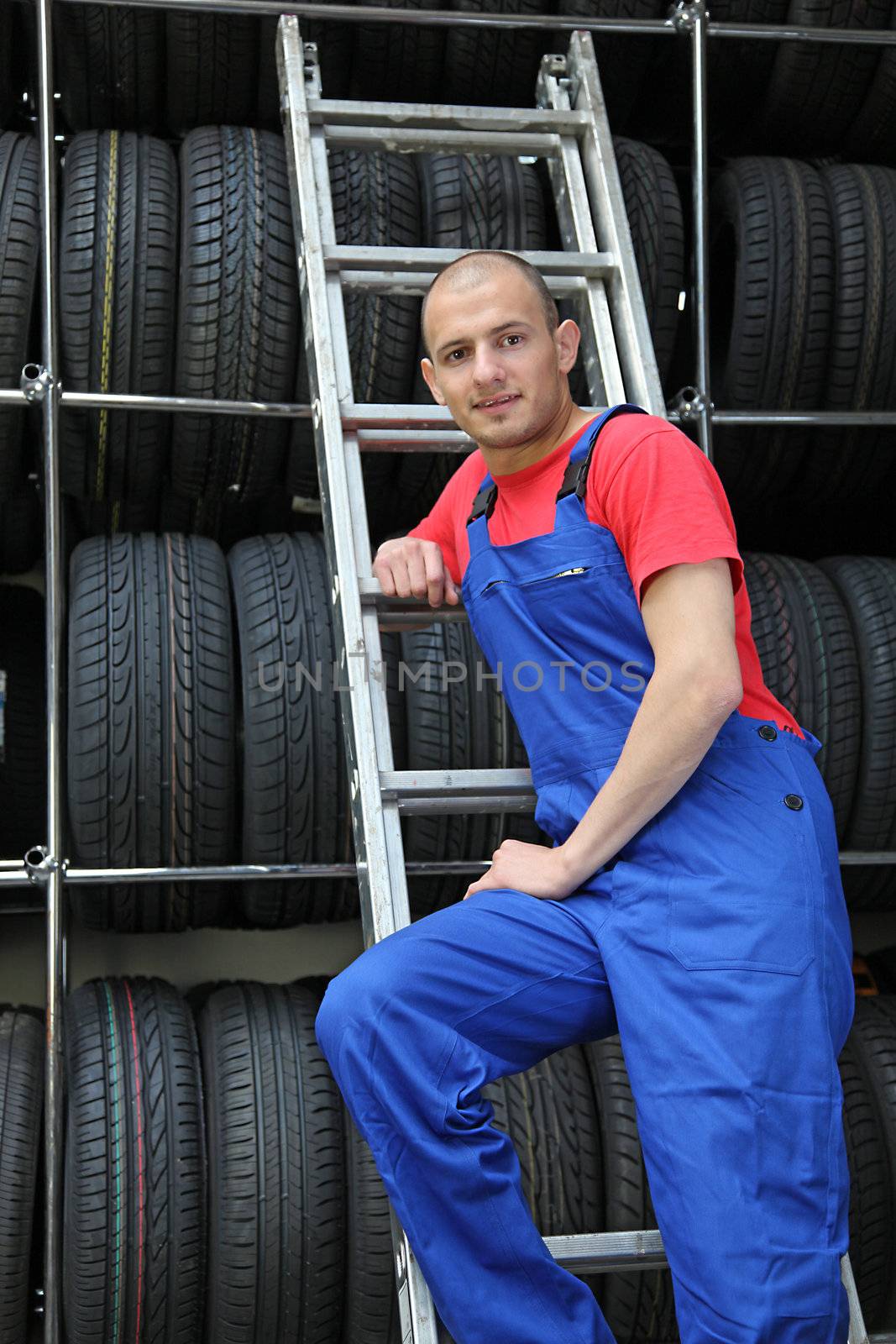 A motivated worker in a tire workshop standing on a ladder.