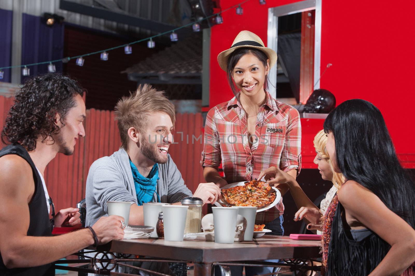 Five laughing friends sharing plate of pizza