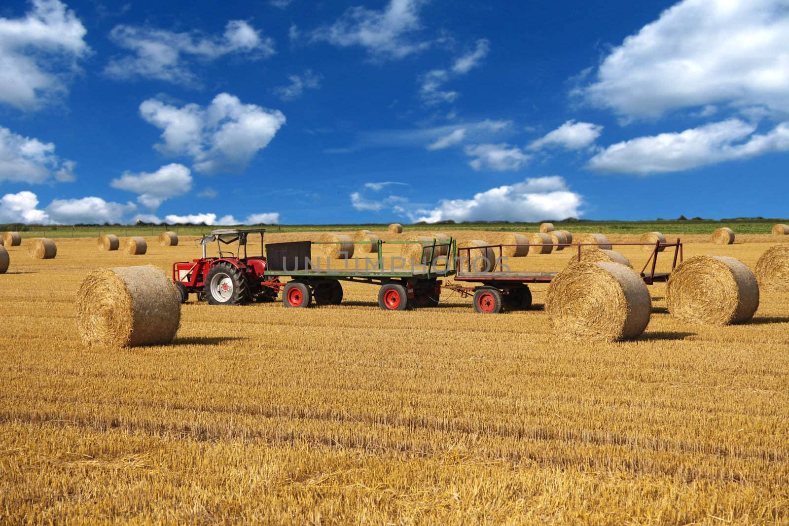 A wide open field showing some bales of straw.