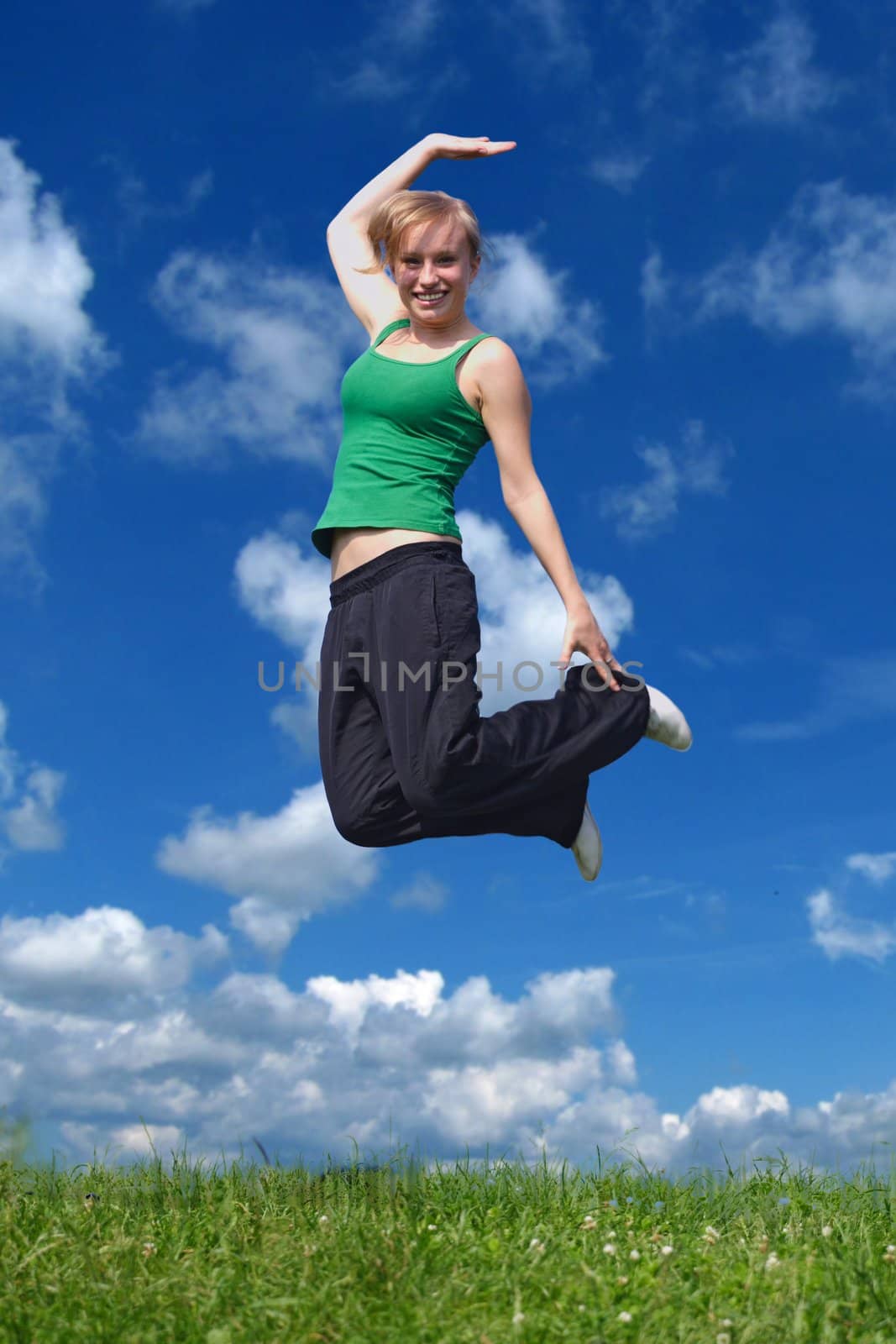 A young attractive woman jumping on a meadow in front of a bright blue sky.