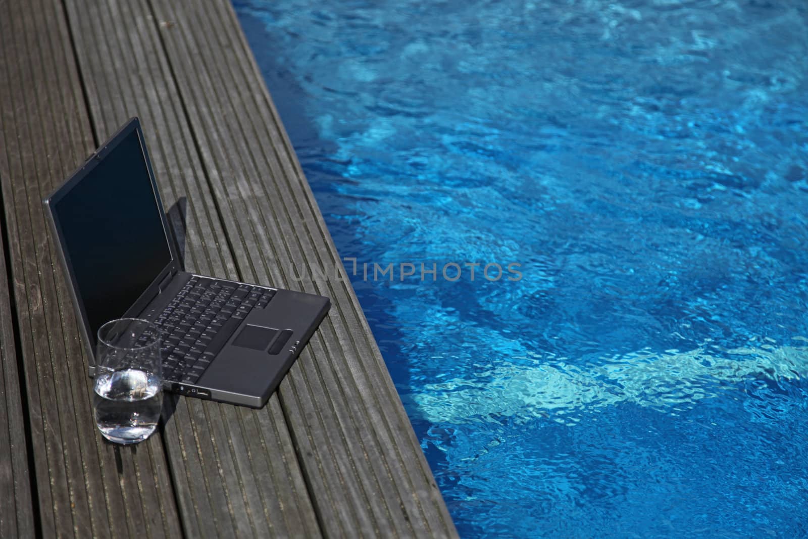 A notebook computer lying next to a swimming pool.