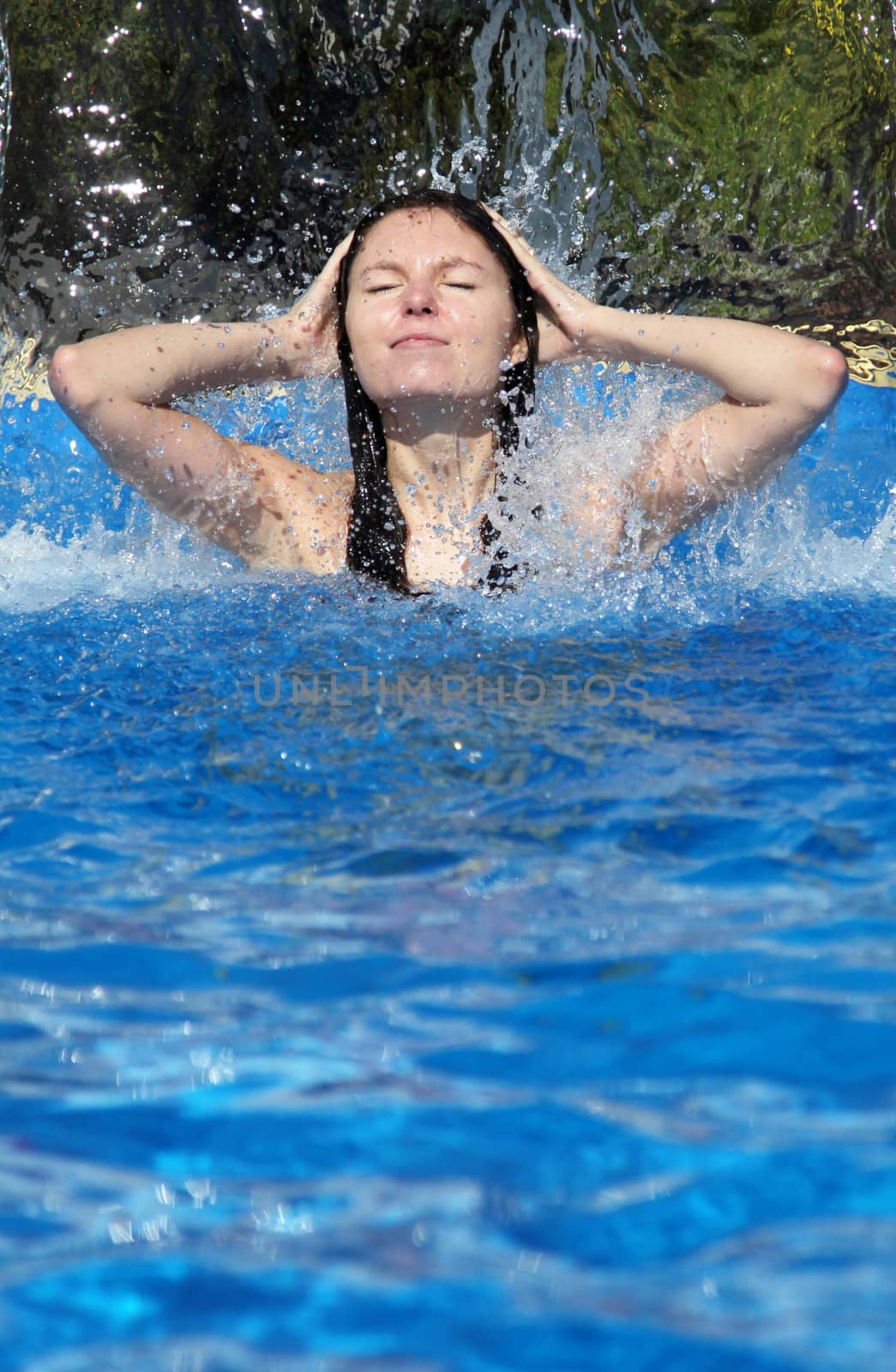 An attractive young woman taking a shower under an artificial waterfall.