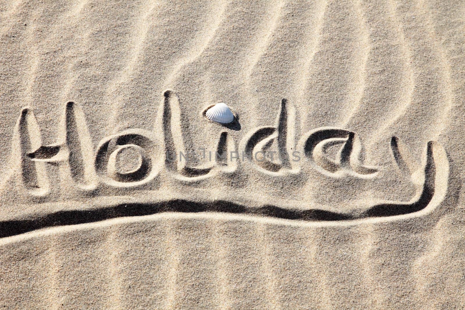 Holiday written in golden sand on a beach.