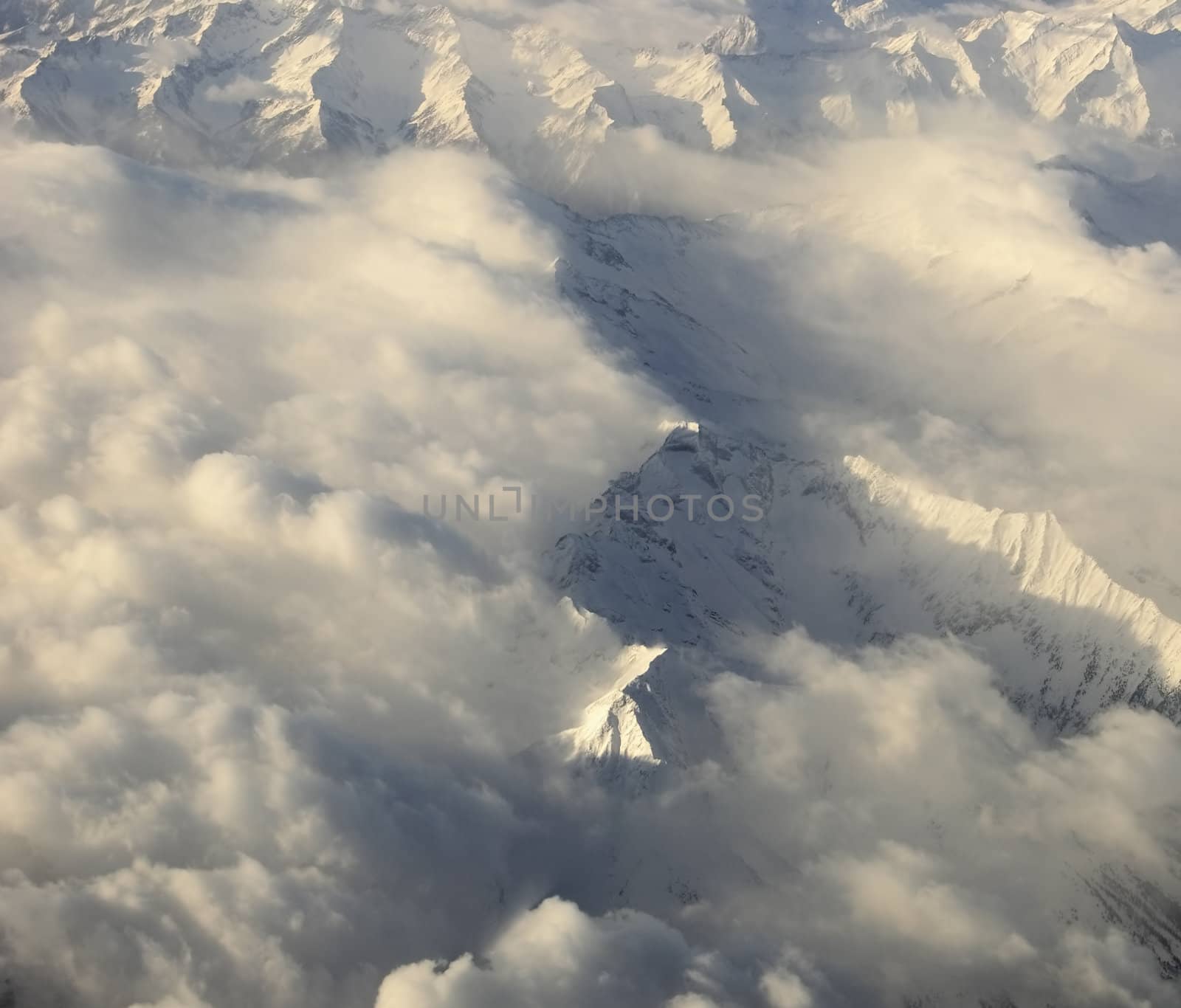 Aerial view of snowy mountains almost covered by clouds just before sunset