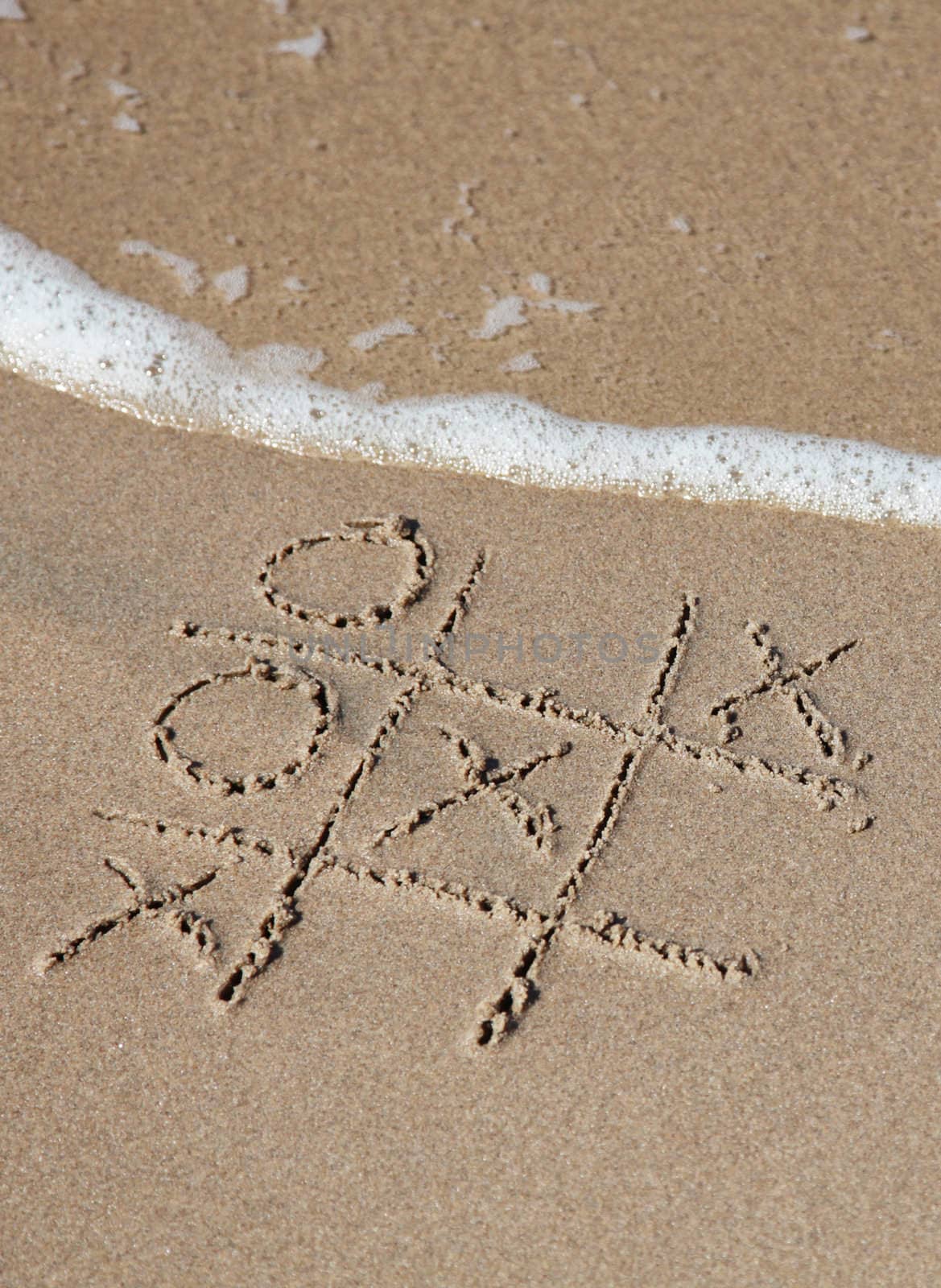 A tic tac toe game drawn in the sand on the beach.