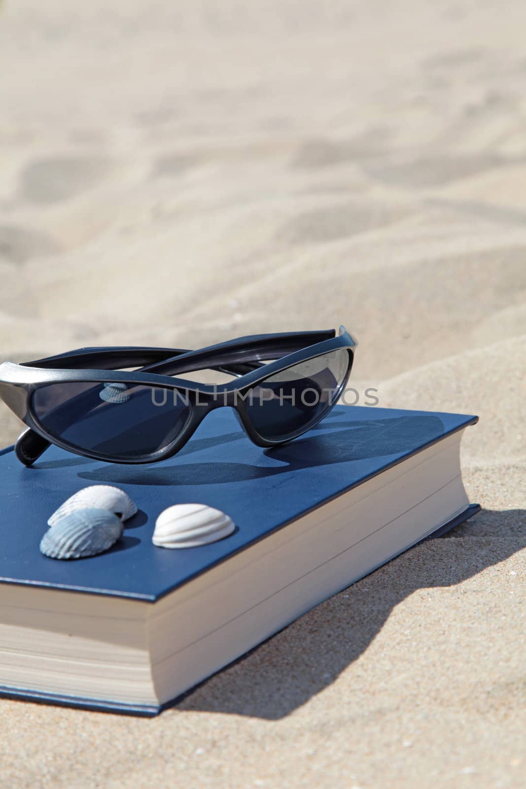 A book and sunglasses lying in the sand, symbolizing recreation.