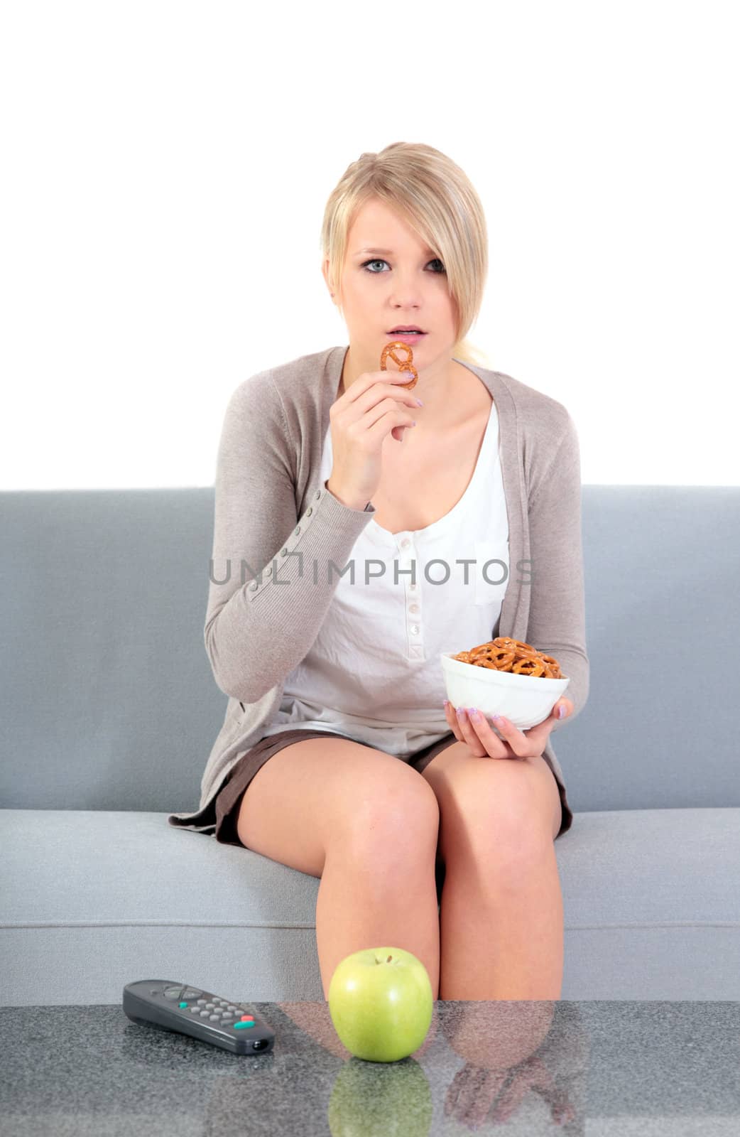 An attractive young woman watching tv and eating snacks while sitting on a couch.