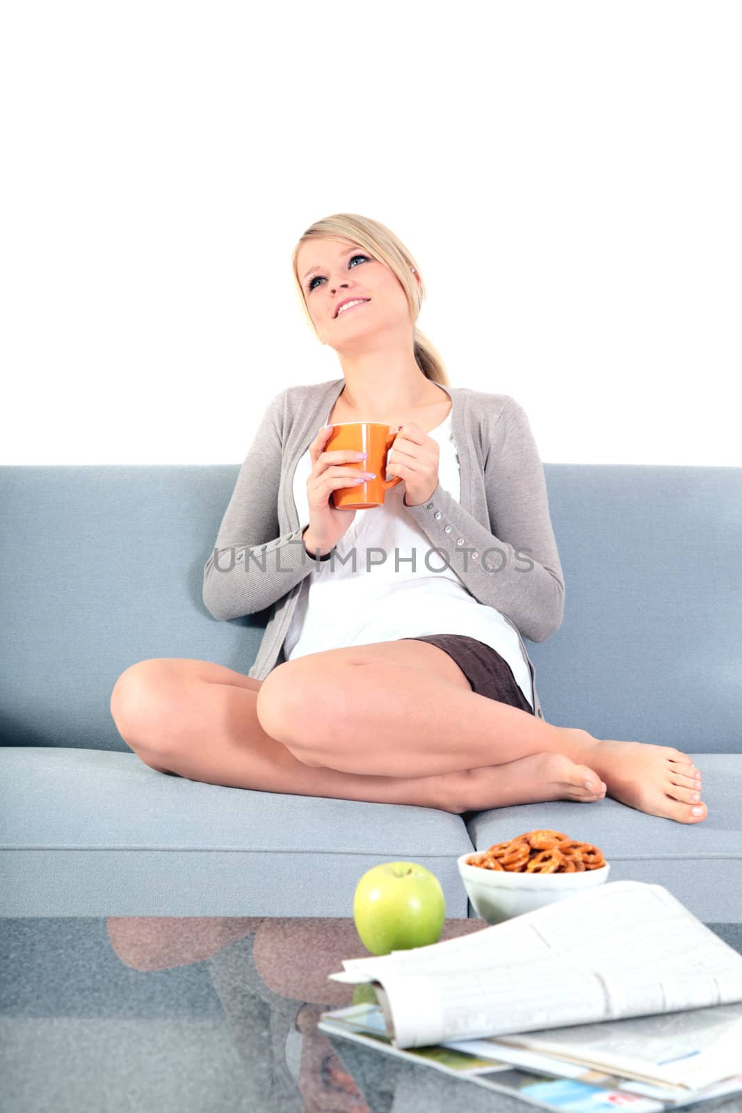 An attractive young woman enjoys a cup of coffee while sitting on a couch.