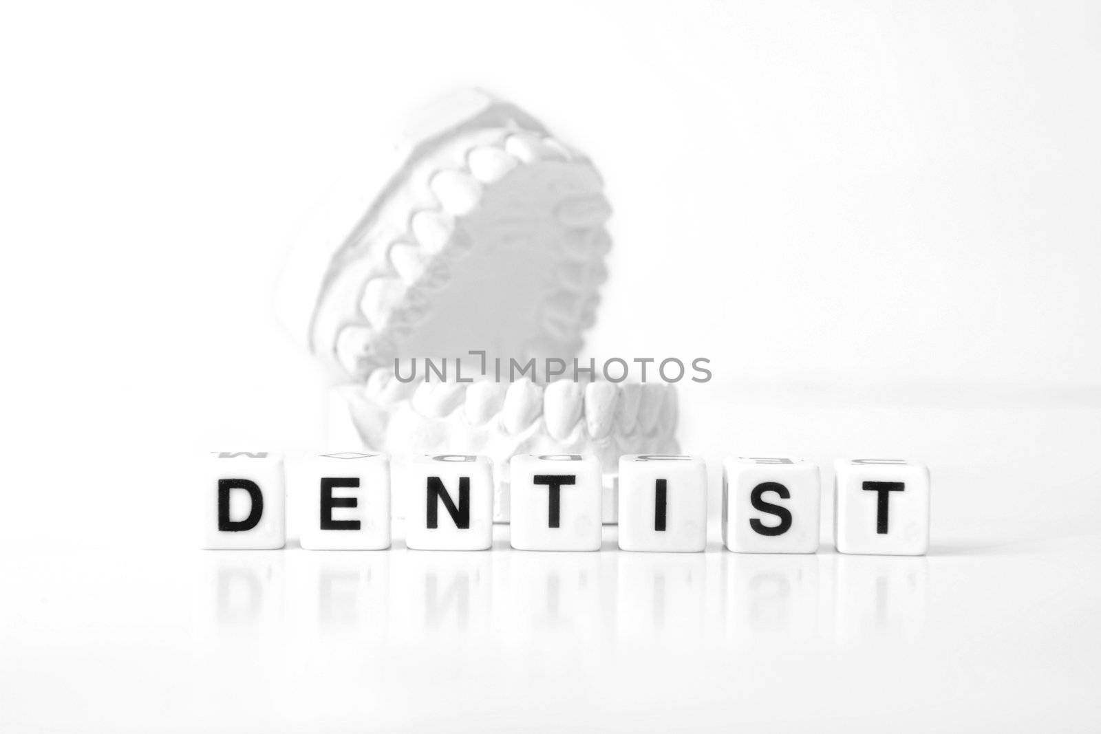 A plaster cast of teeth behind several dices that form the word dentist. All on white background.